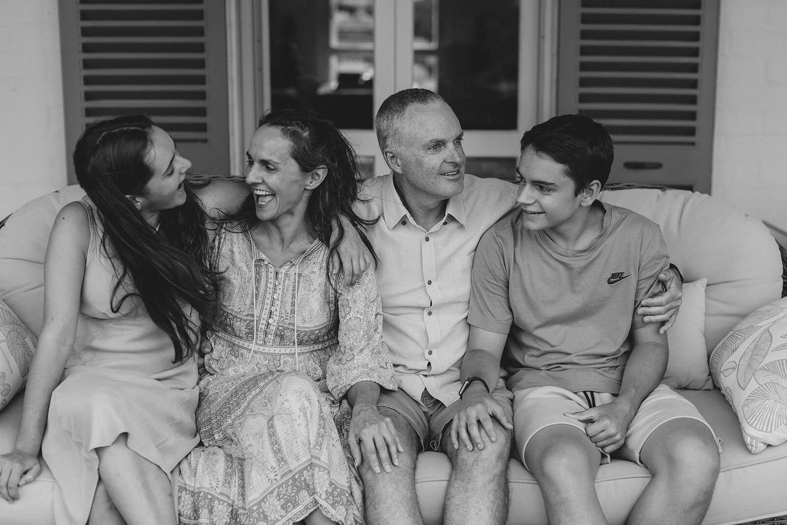 Black and white photo of a family of four laughing together on the verandah couch
