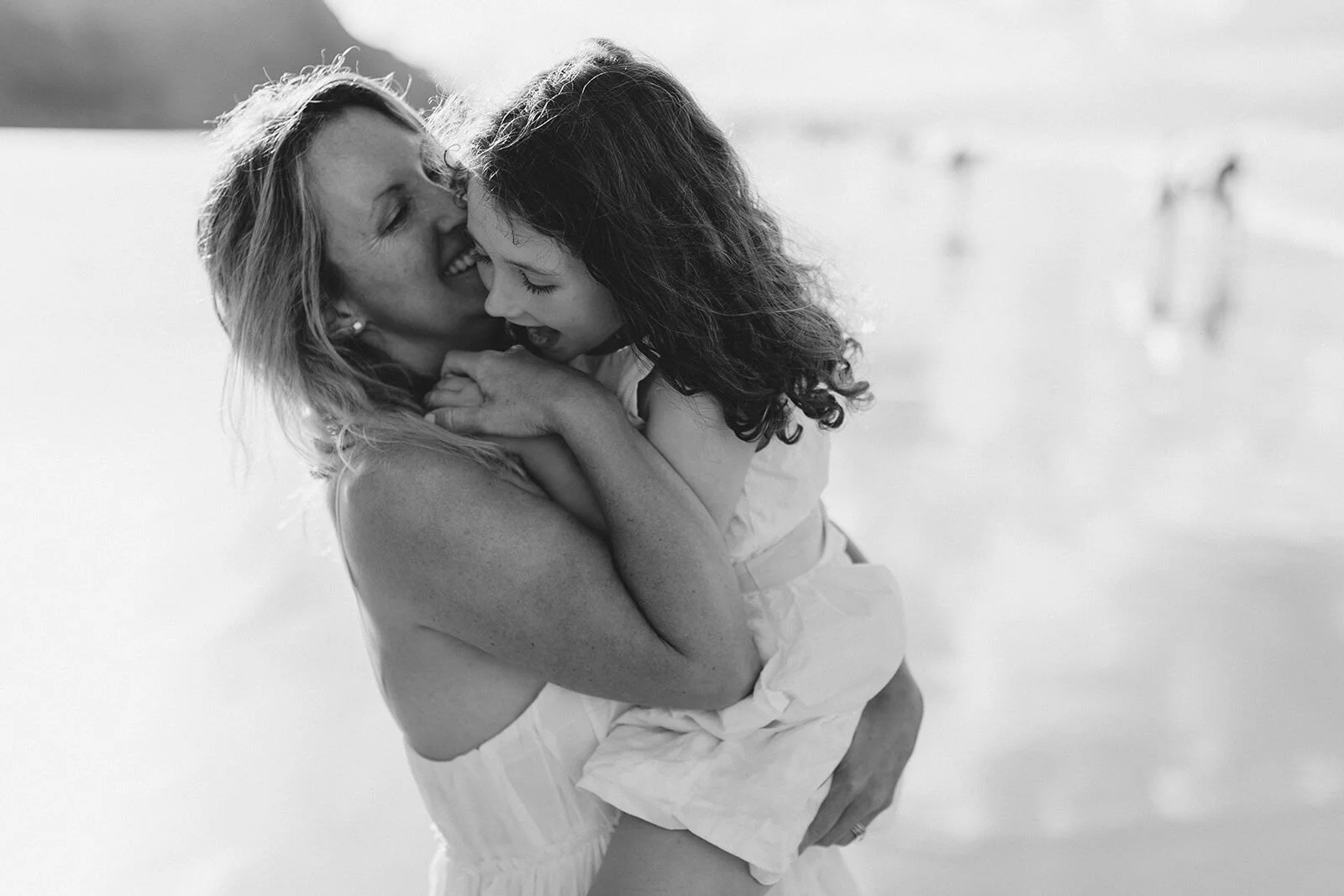 Black and white photo of mum cuddling her daughter in her arms at the water's edge