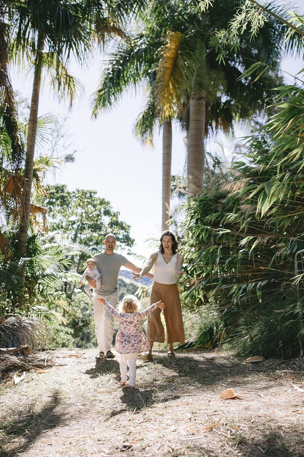 Parents walking toward the camera holding their toddler's hands, framed by palm trees