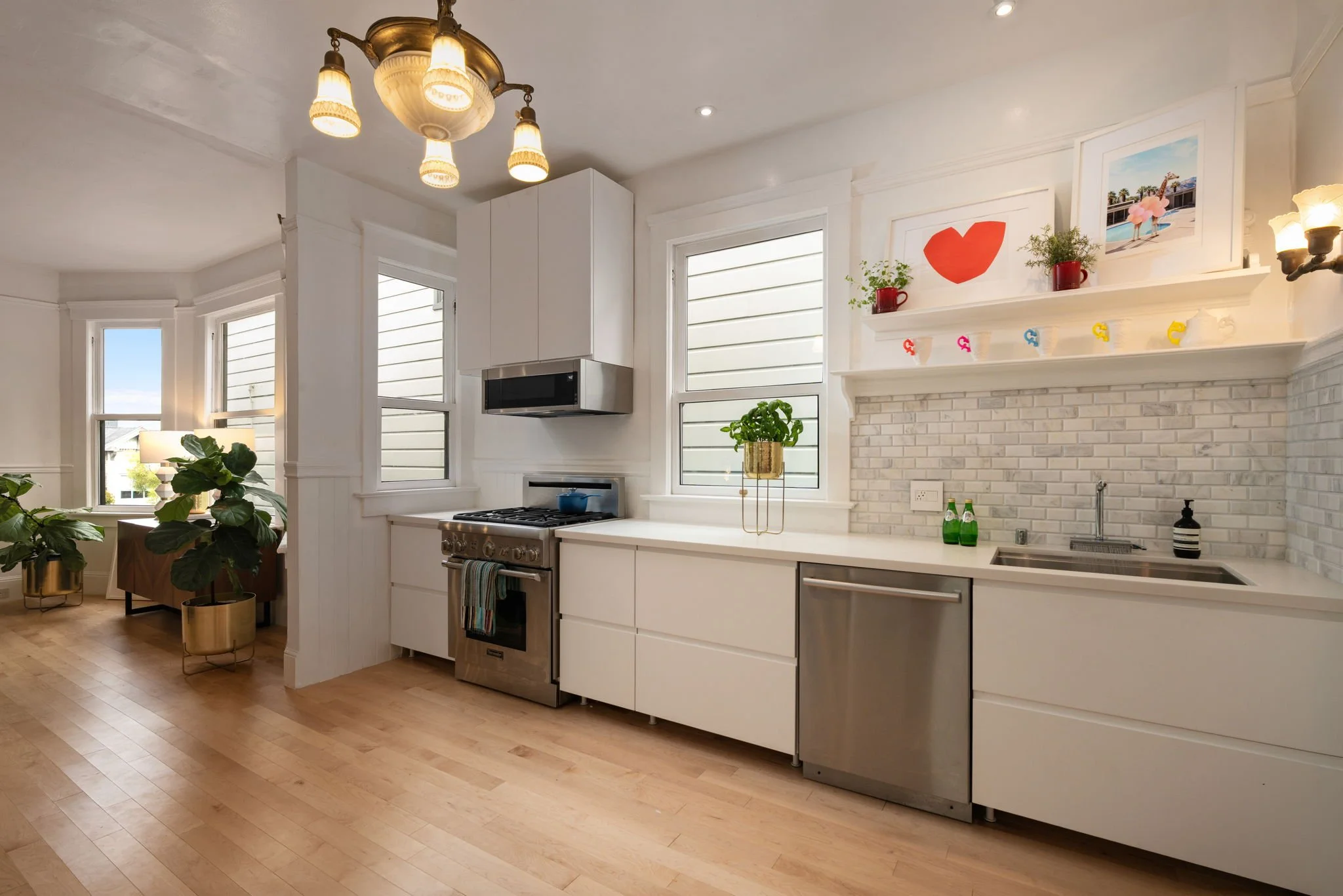 Modern kitchen with white cabinets, stainless steel stove, white brick backsplash, and framed art above the fireplace.