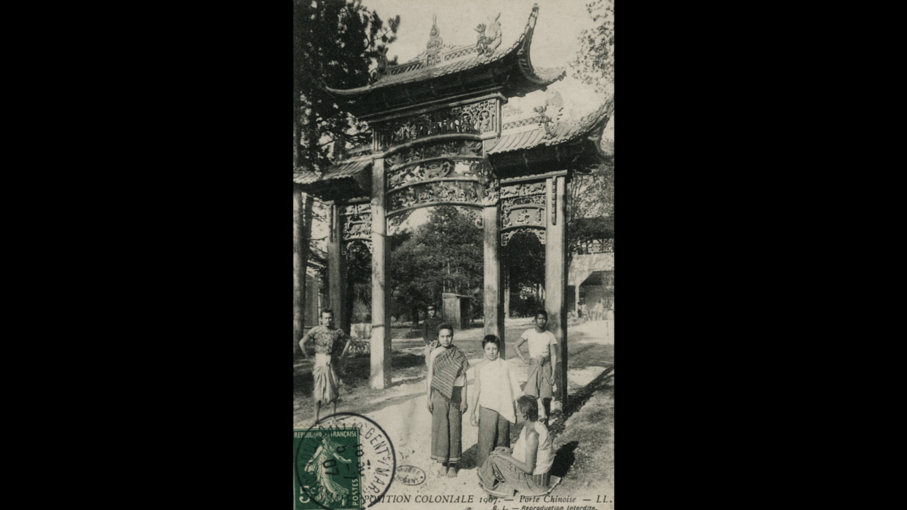Une photographie en noir et blanc montrant une porte chinoise traditionnelle, intitulée 'Porte Chinoise' en 1907, avec quatre personnes, dont deux femmes et deux hommes, posant devant. La scène est en plein air avec des arbres en arrière-plan.