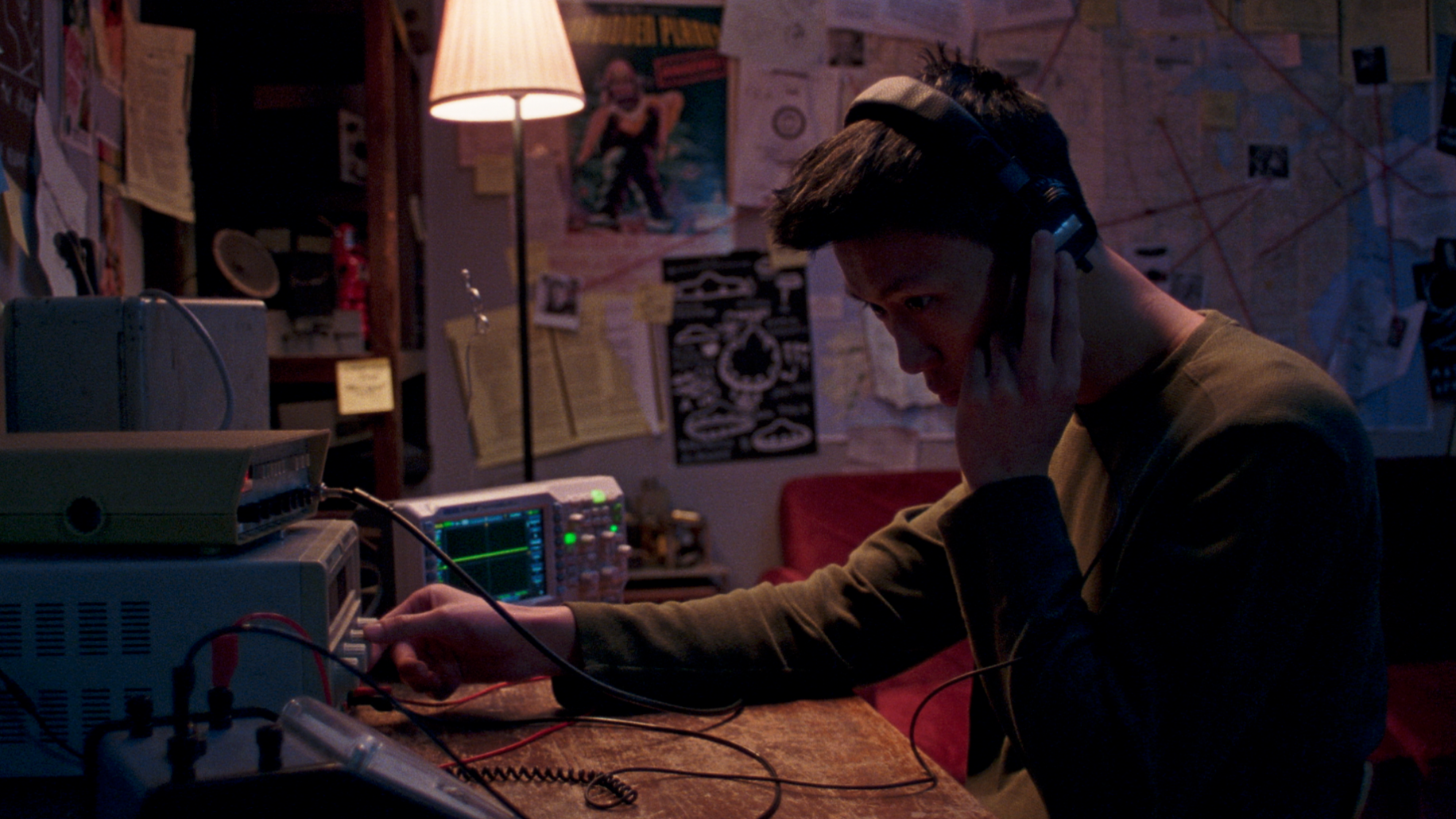 Jeune homme travaillant en studio de musique avec casque, entouré d'équipement audio et décor murale colorée