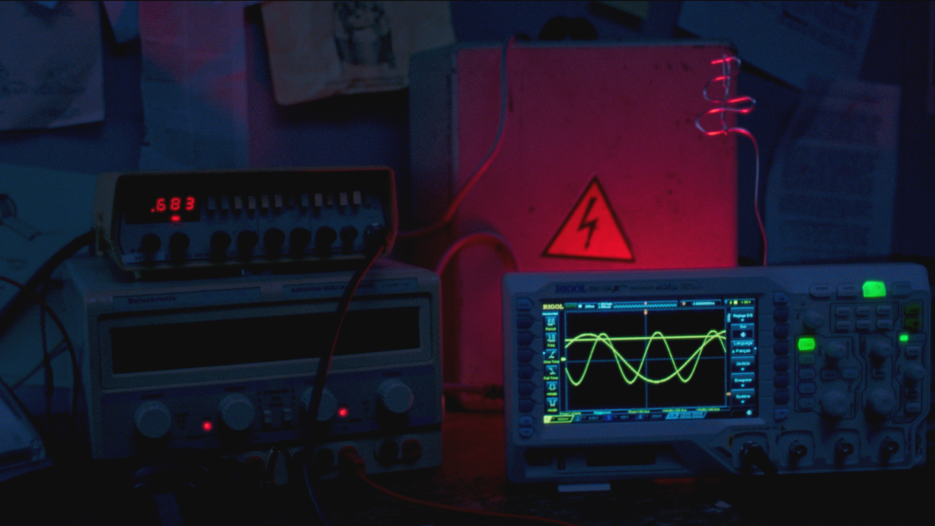 Configuration expérimentale avec oscilloscopes et générateur de signaux, affichant des courbes sinusoïdales lumineuses en noir et vert, avec un symbole de danger électrique, dans un environnement de laboratoire.