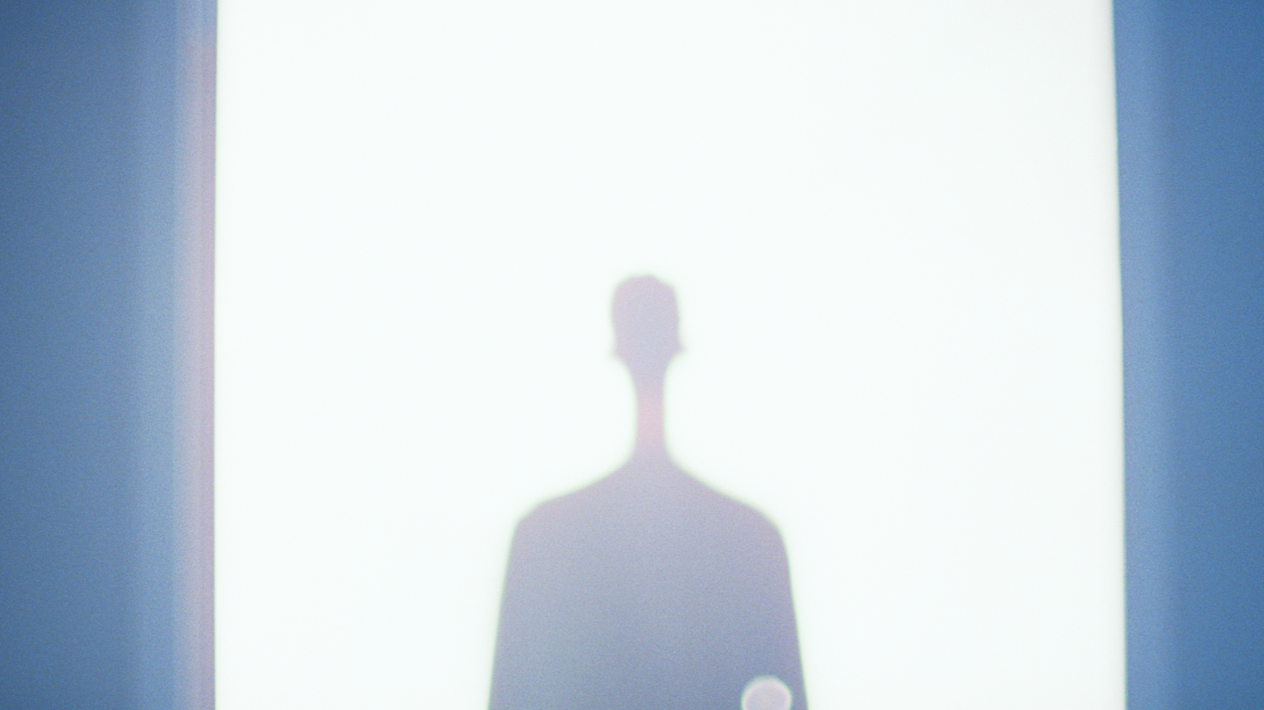 Silhouette d'une personne vue en contre-jour, projetée sur un mur blanc, entourée d'un cadre bleu.