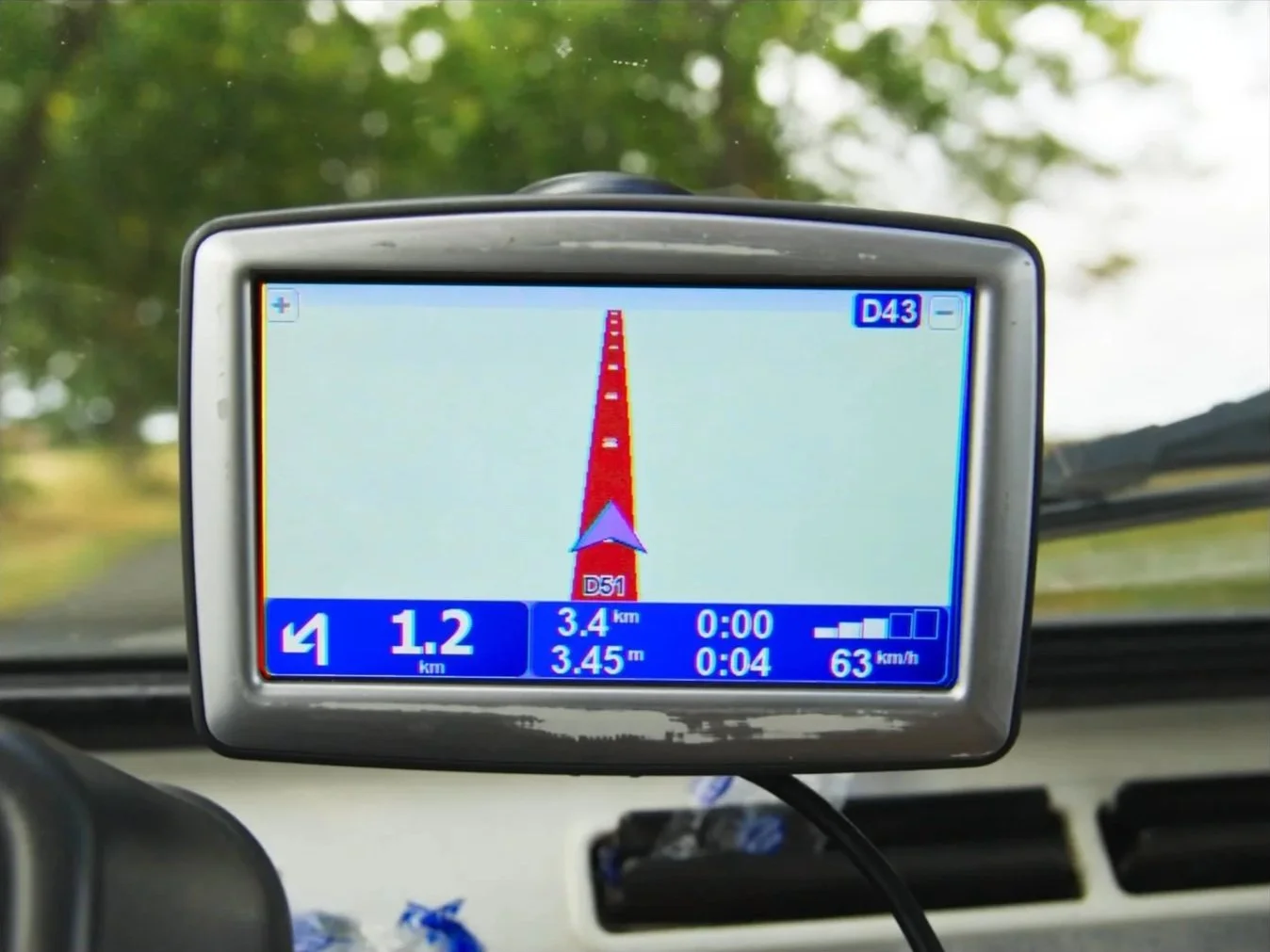 GPS de voiture affichant une carte avec une route droite. La vitesse indiquée est de 63 km/h, avec une distance restante de 1,2 km. La carte montre la route D51, D43, et d'autres informations de navigation.