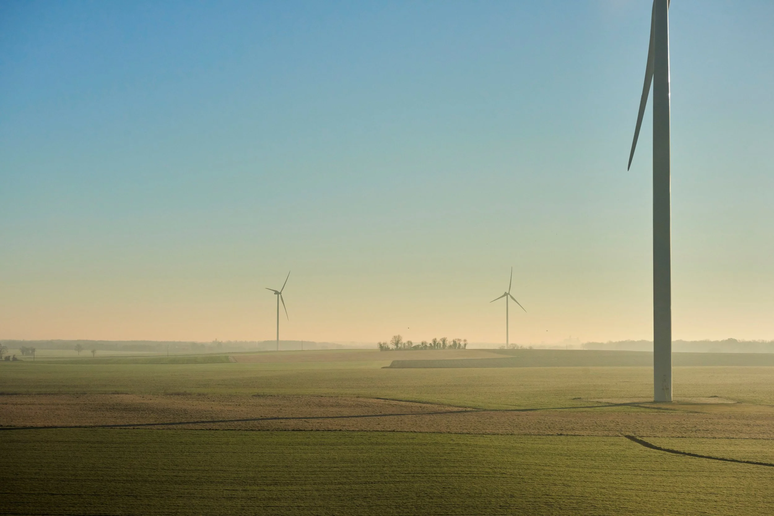 Paysage agricole avec des turbines éoliennes dans un champ ouvert, ciel clair en arrière-plan.