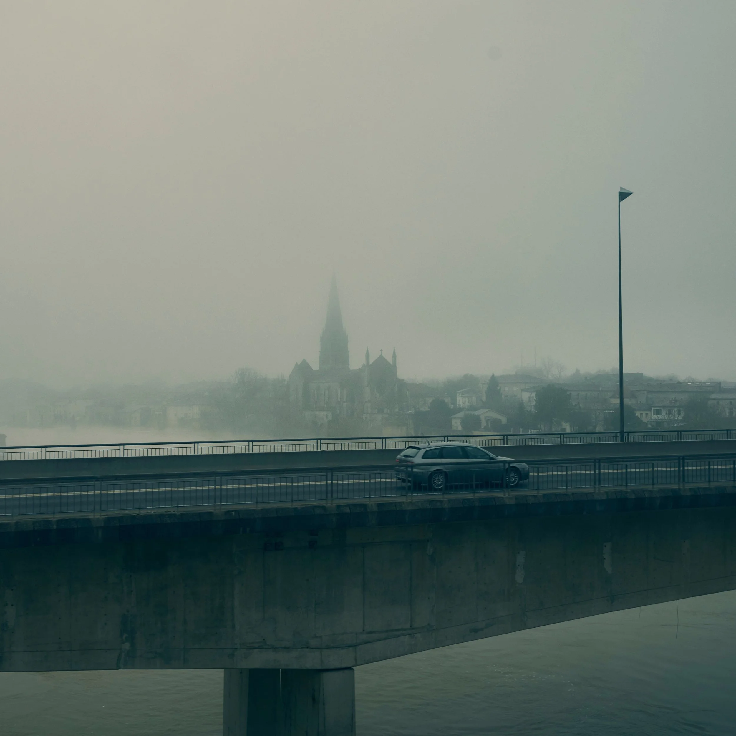 Une vue depuis une fenêtre montrant une ville en brume avec un bâtiment emblématique en forme de spire au centre, deux lampadaires de part et d'autre et une voiture au premier plan.
