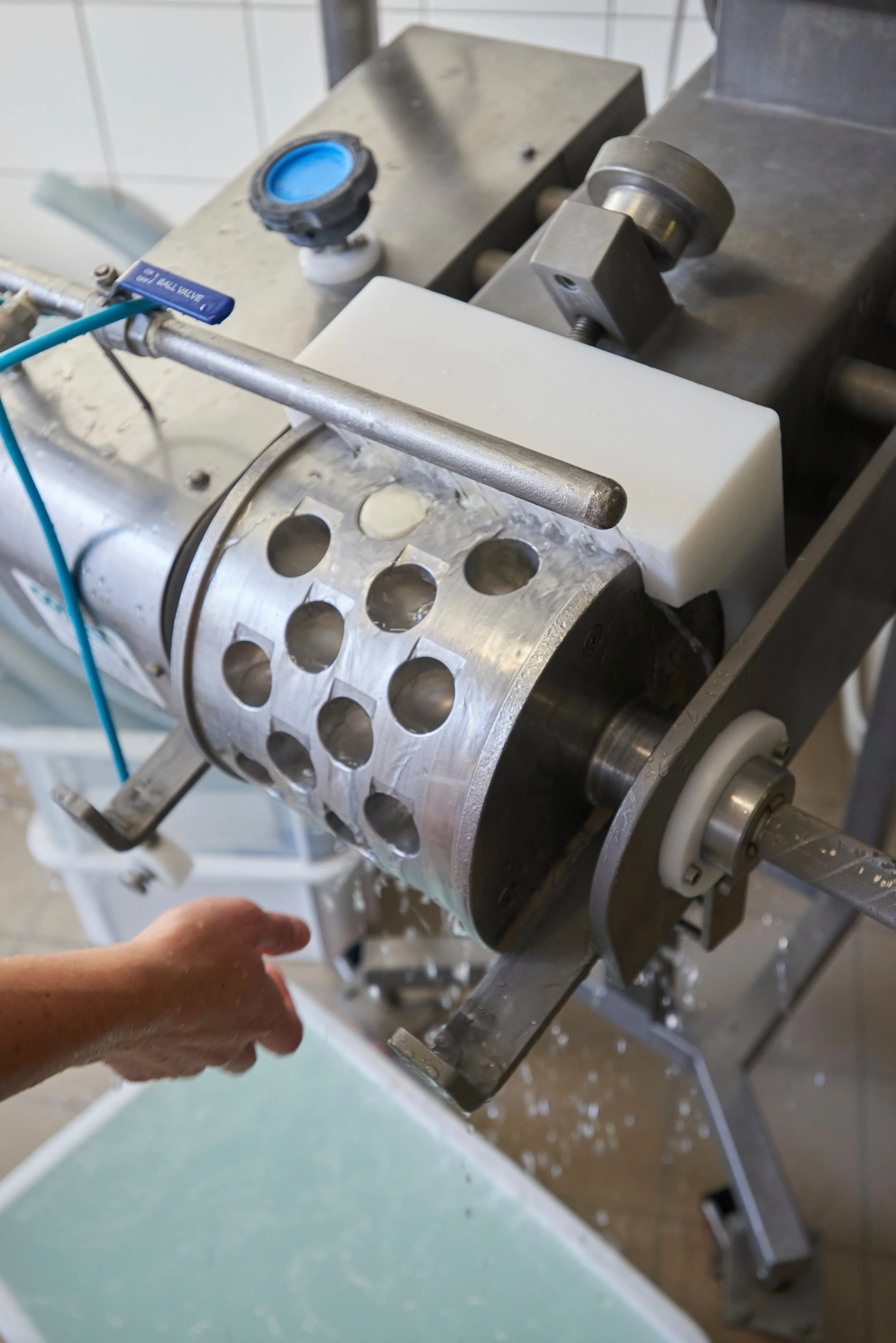 Un équipement industriel en métal, possédant une valve de boule en plastique bleu, dans une zone propre et bien éclairée, avec un fond en carrelage blanc.