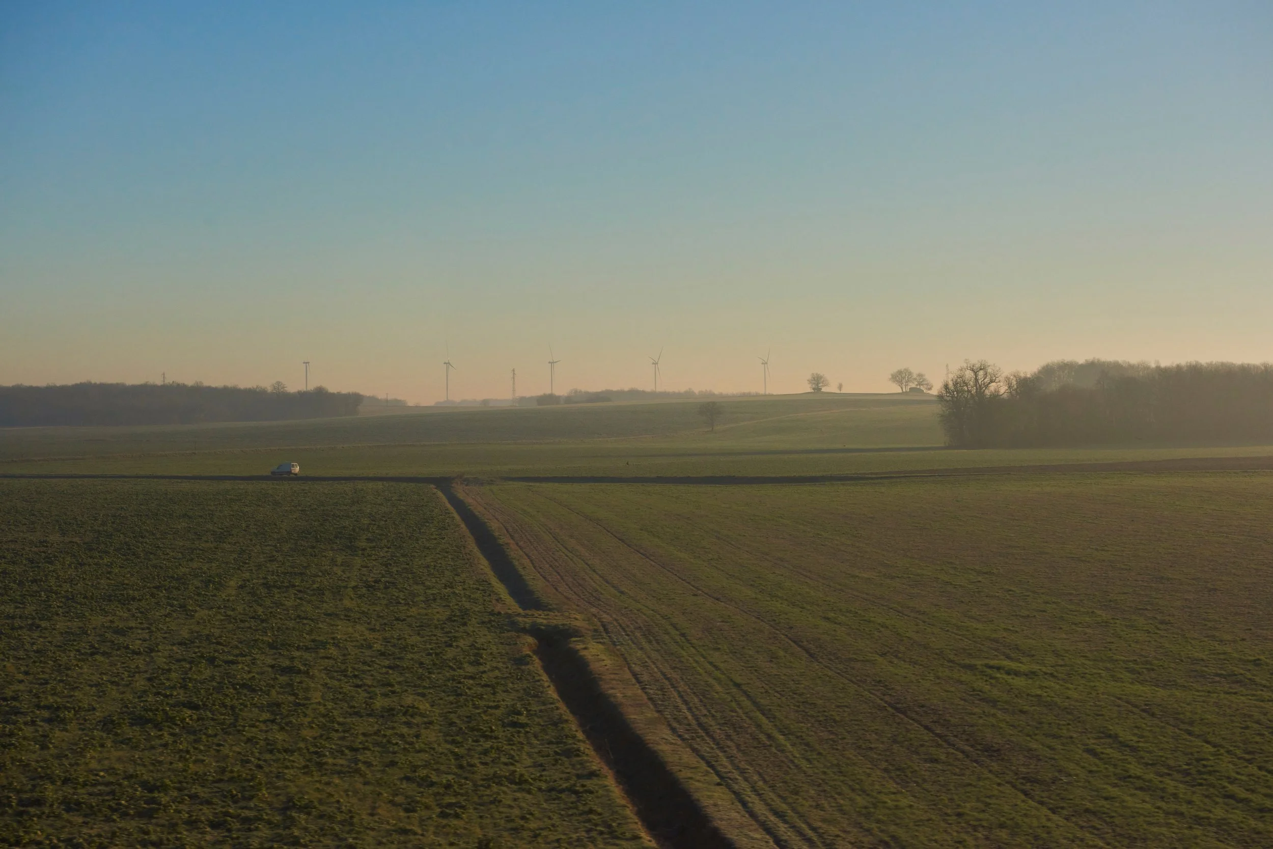 Paysage de champs agricoles avec des éoliennes au loin sous un ciel clair.
