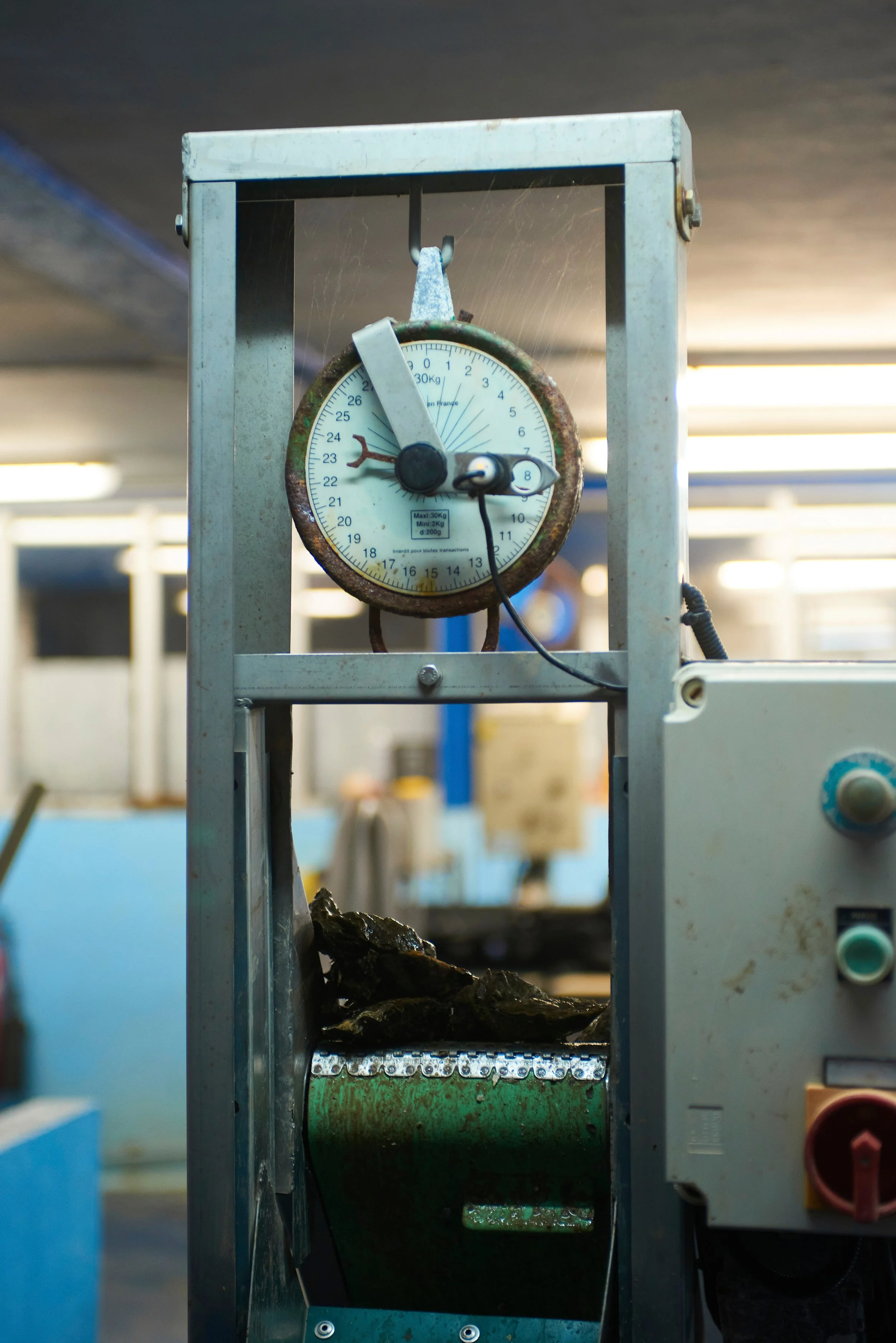 Une machine de test de déformation mécanique avec un cadran indiquant 0, une roche posée sur la machine, dans un environnement industriel avec des lumières au plafond.