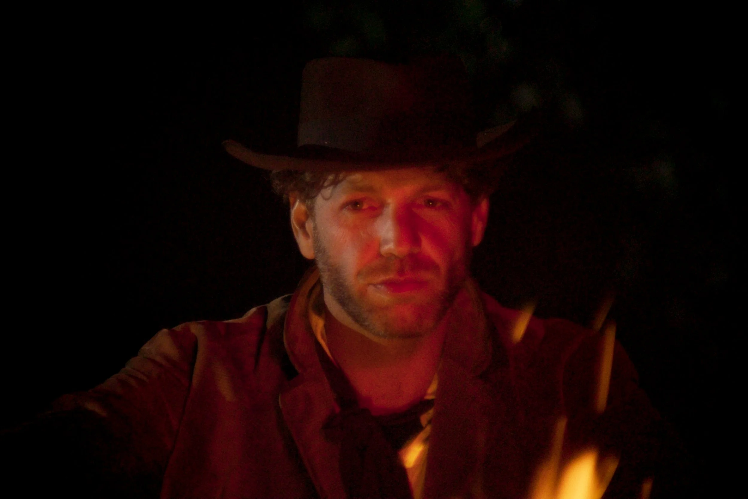Portrait d'un homme portant un chapeau noir, dans un environnement sombre avec un éclairage rouge et jaune