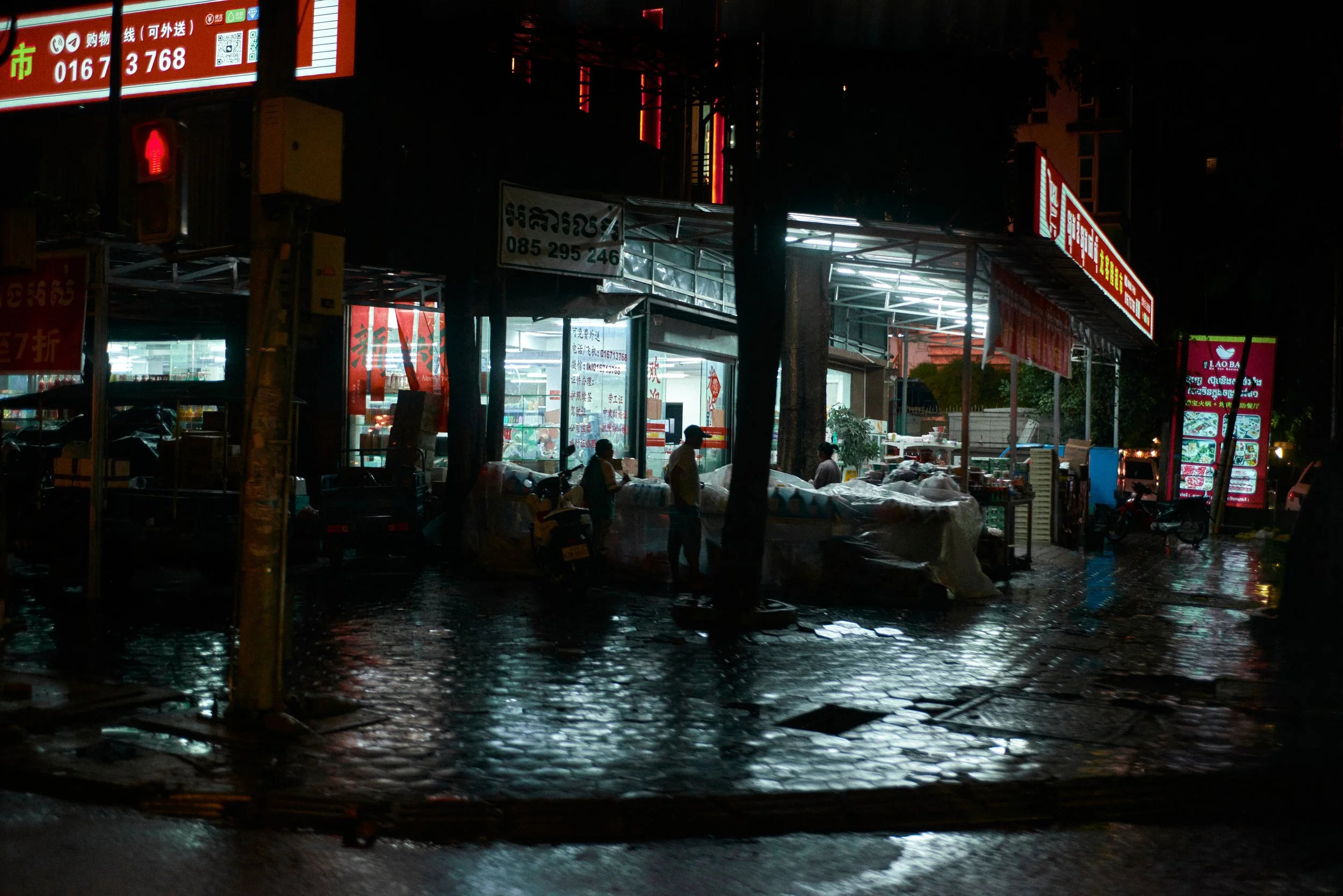 Rue commerçante enneigée la nuit, éclairée par des enseignes lumineuses rouges et blanches, avec des passants et des véhicules.