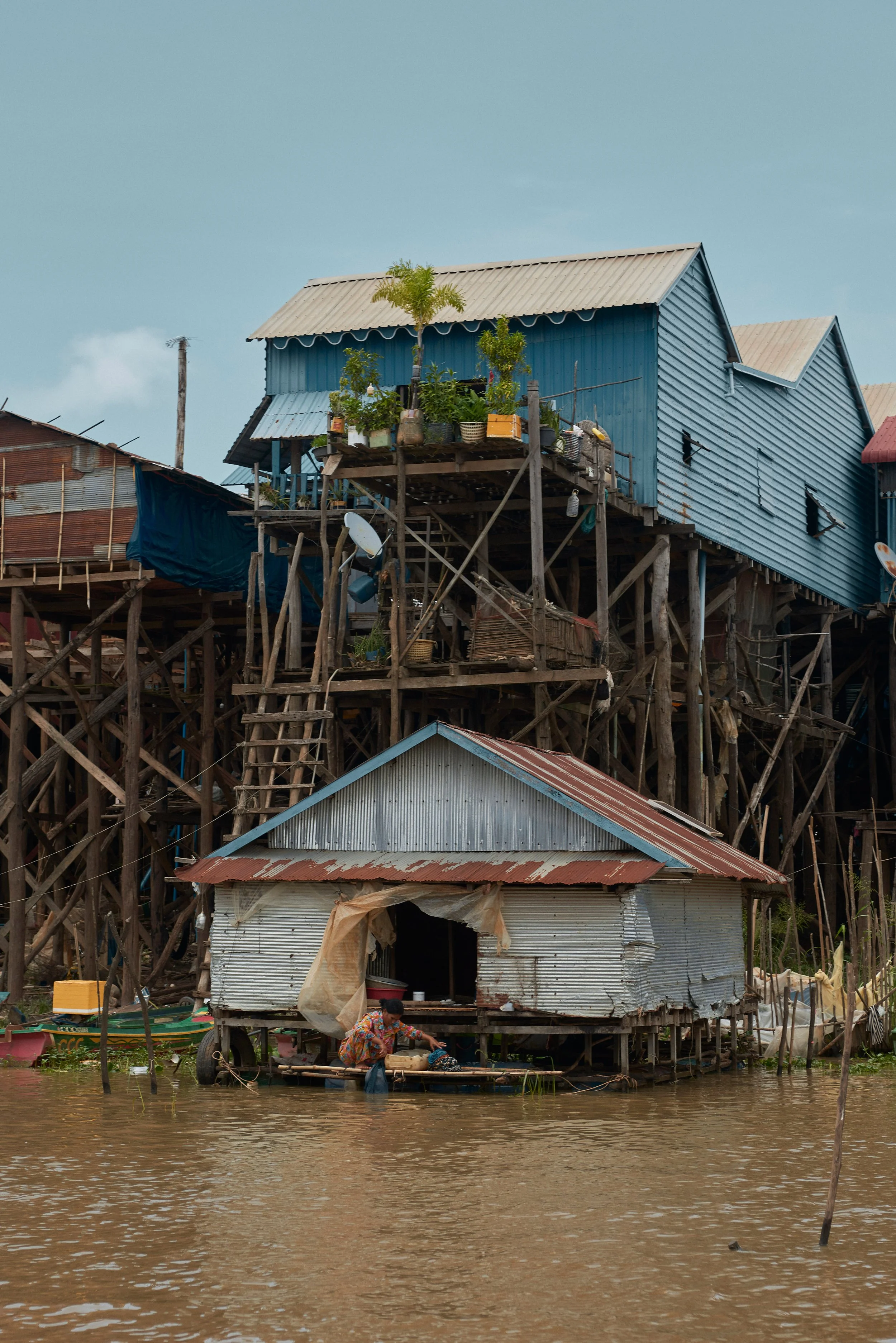 Une maison en bois flottant sur l'eau, avec une personne dans une barque devant, dans un environnement humide ou inondé.