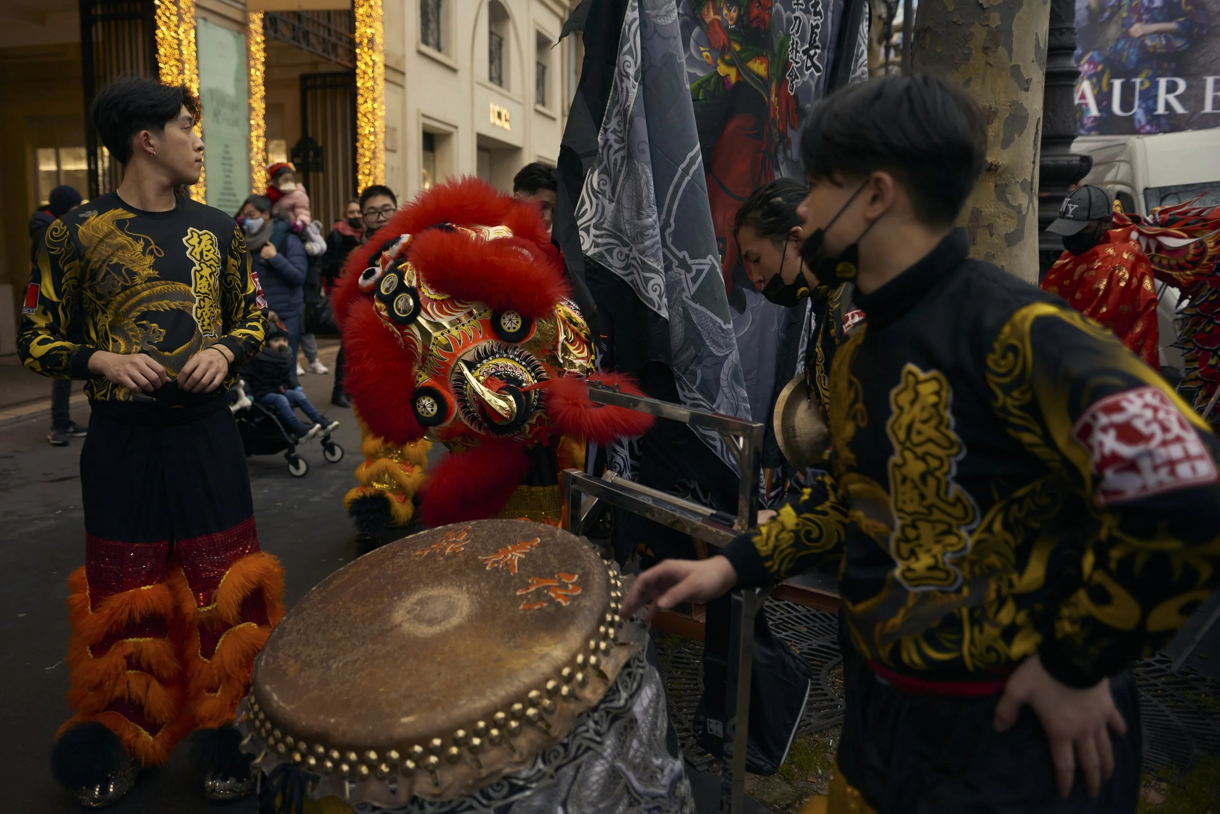 Groupe de personnes participant à une parade ou cérémonie avec un lion traditionnel chinois en costume coloré, entourés de spectateurs dans une rue illuminée.