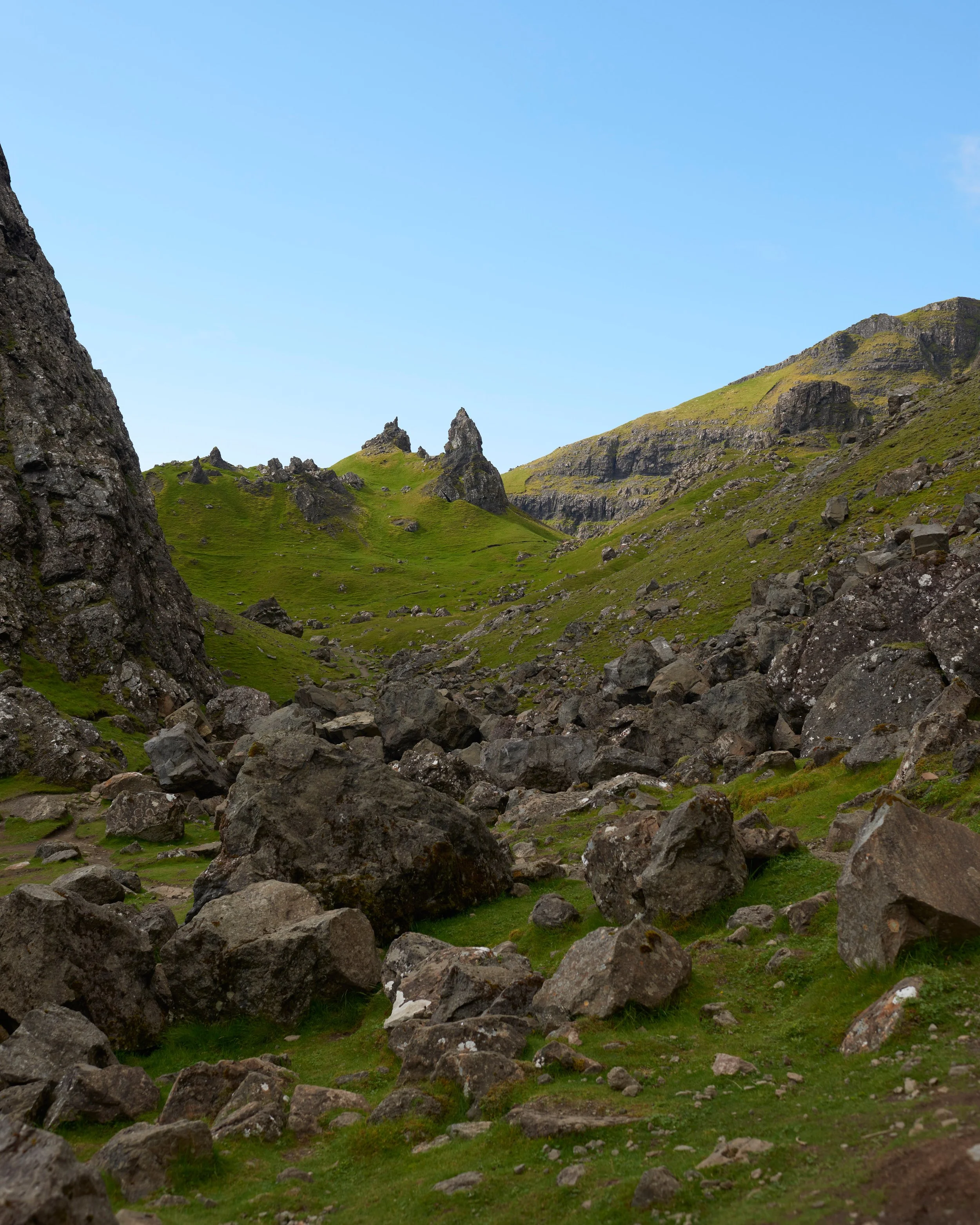 Paysage de montagnes avec des rochers et de l'herbe verte sous un ciel bleu clair.