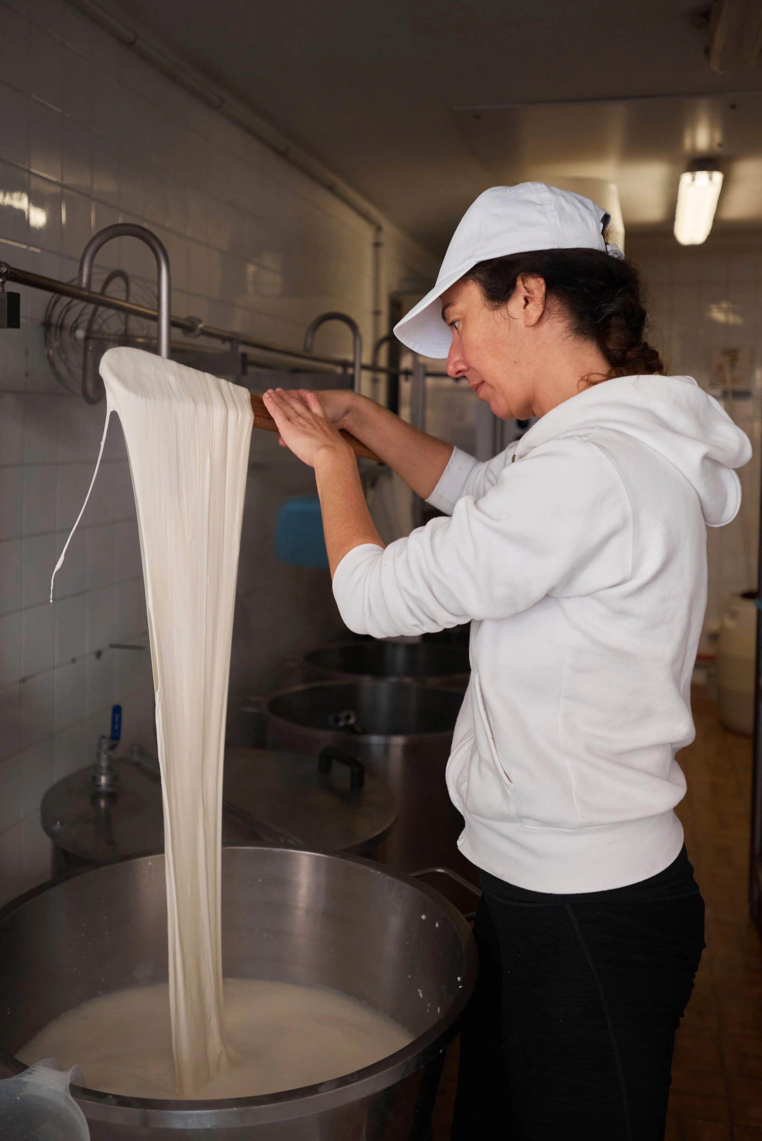 Une femme verse de la pâte à crêpes dans une grande cuve en acier inoxydable, dans une cuisine.