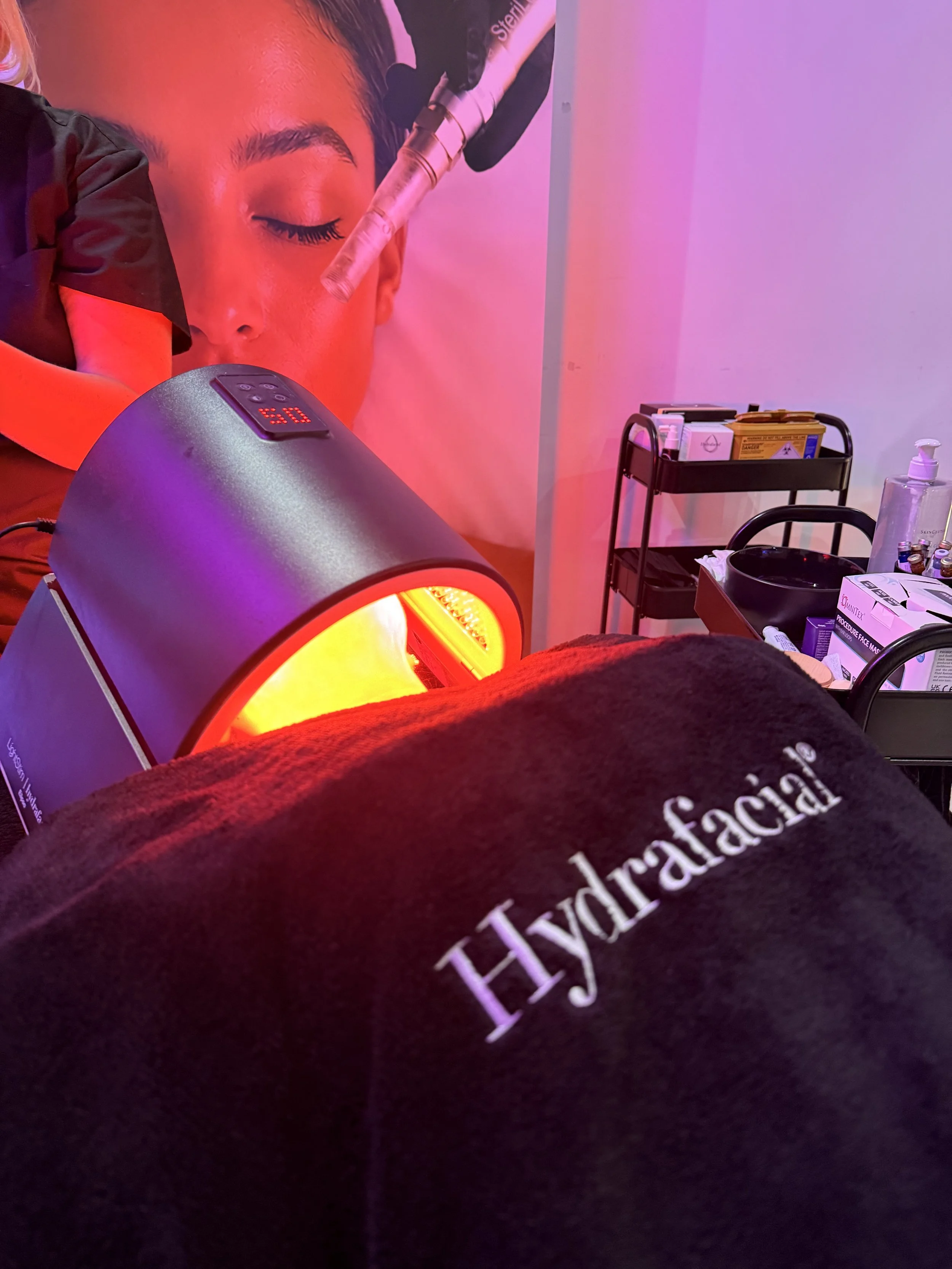 Close-up of a person receiving LED light therapy treatment in a clinic, with medical supplies and equipment on a cart in the background.