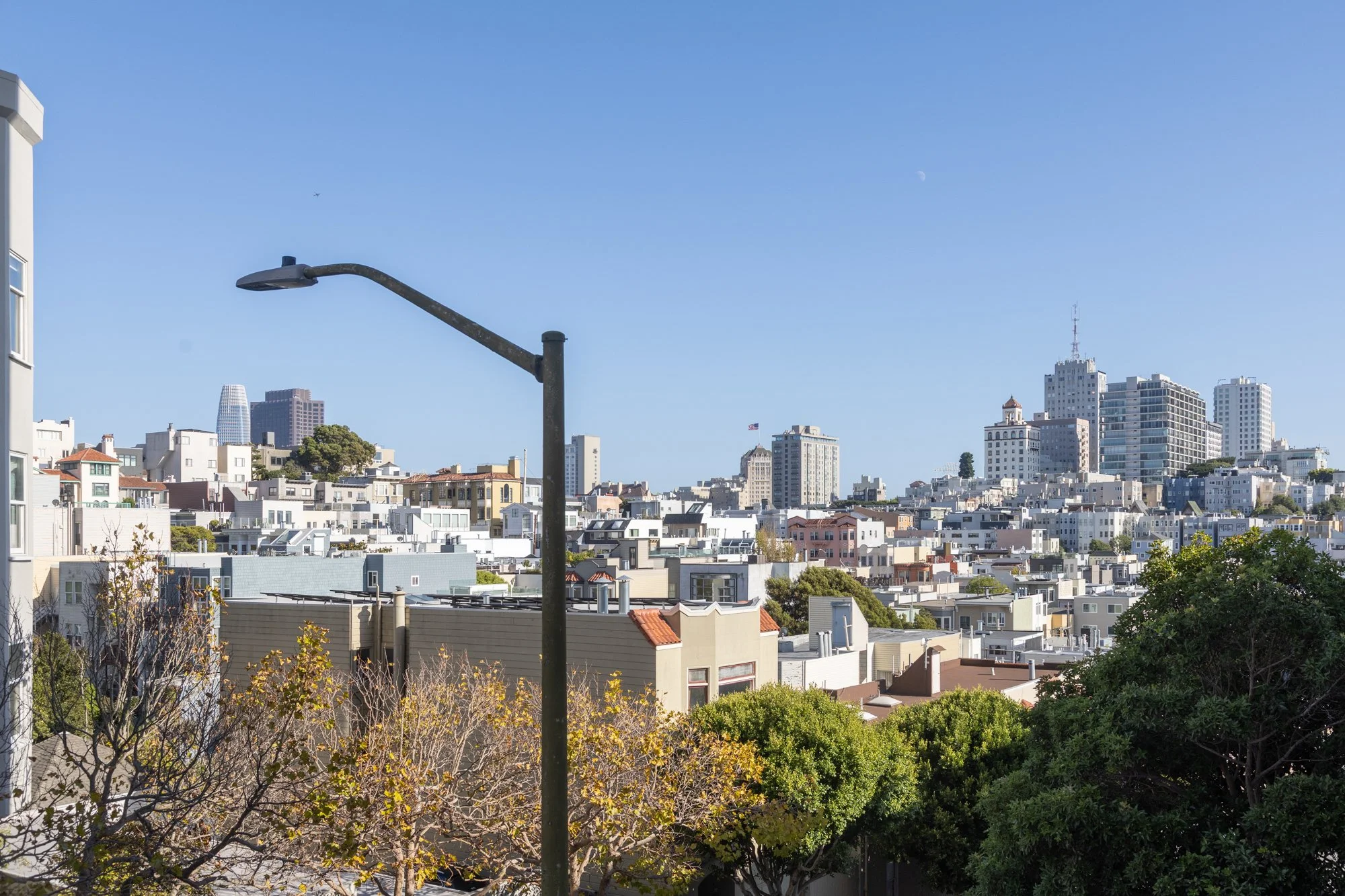 View of a city skyline under a clear blue sky with a streetlamp in the foreground and various buildings, including high-rise office buildings and residential houses.