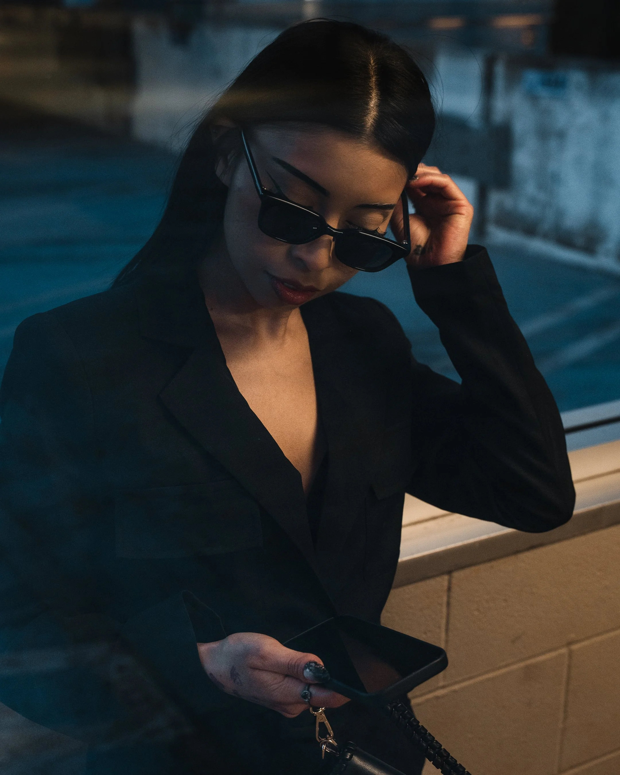 A woman with long dark hair wearing sunglasses and a black top, looking at her phone.