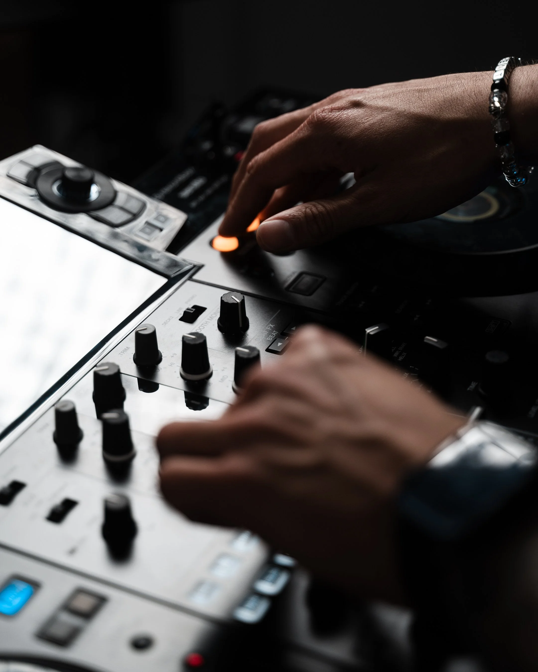 Close-up of a person's hand adjusting the knobs on a DJ mixing console, with a dark background.