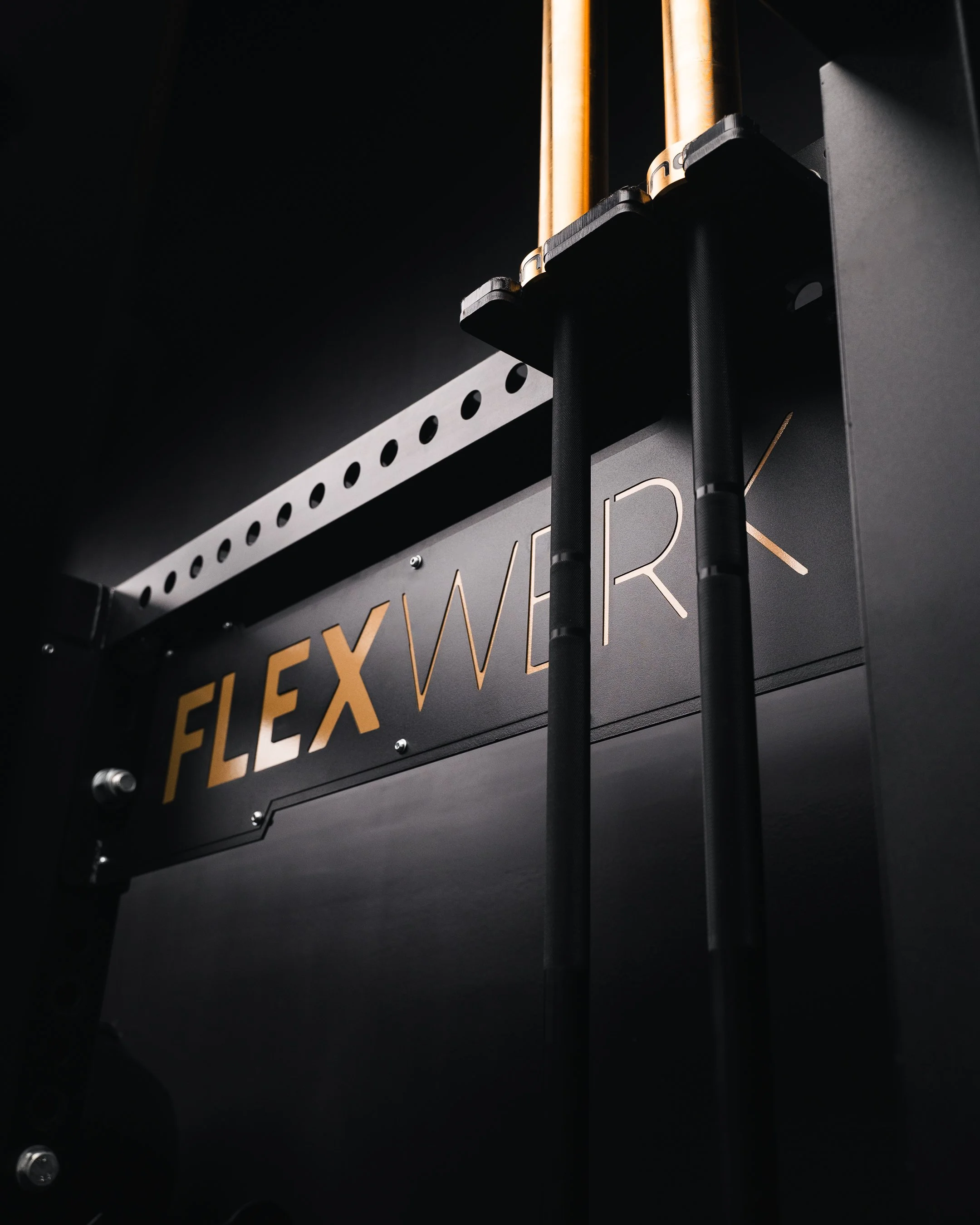 Close-up of a black display with gold lettering that reads 'FLEX' and two vertical black phone-like objects in front of it. The background is dark with minimal lighting.