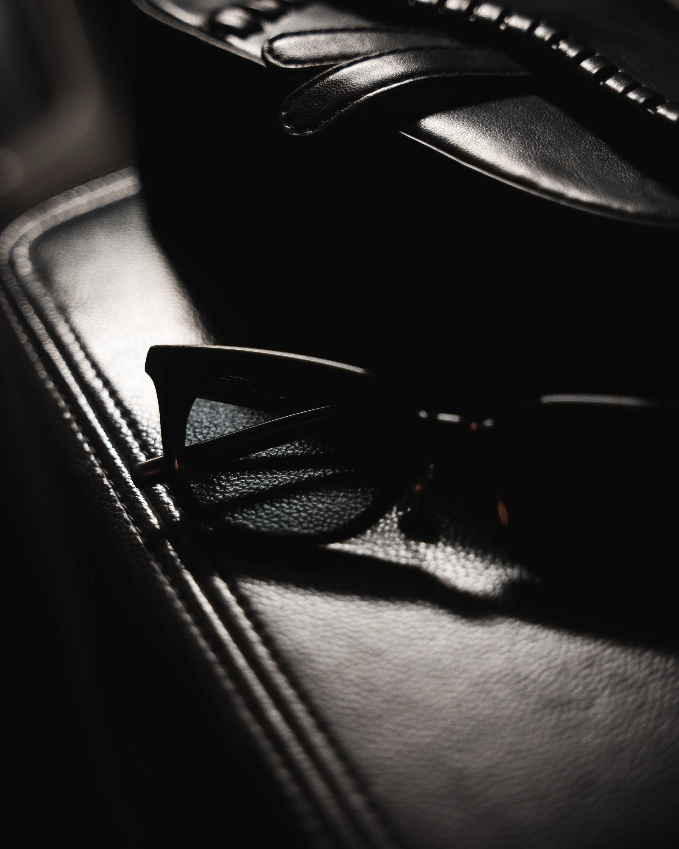 Close-up photo of a black leather strap or harness with details and stitching, taken in low lighting.