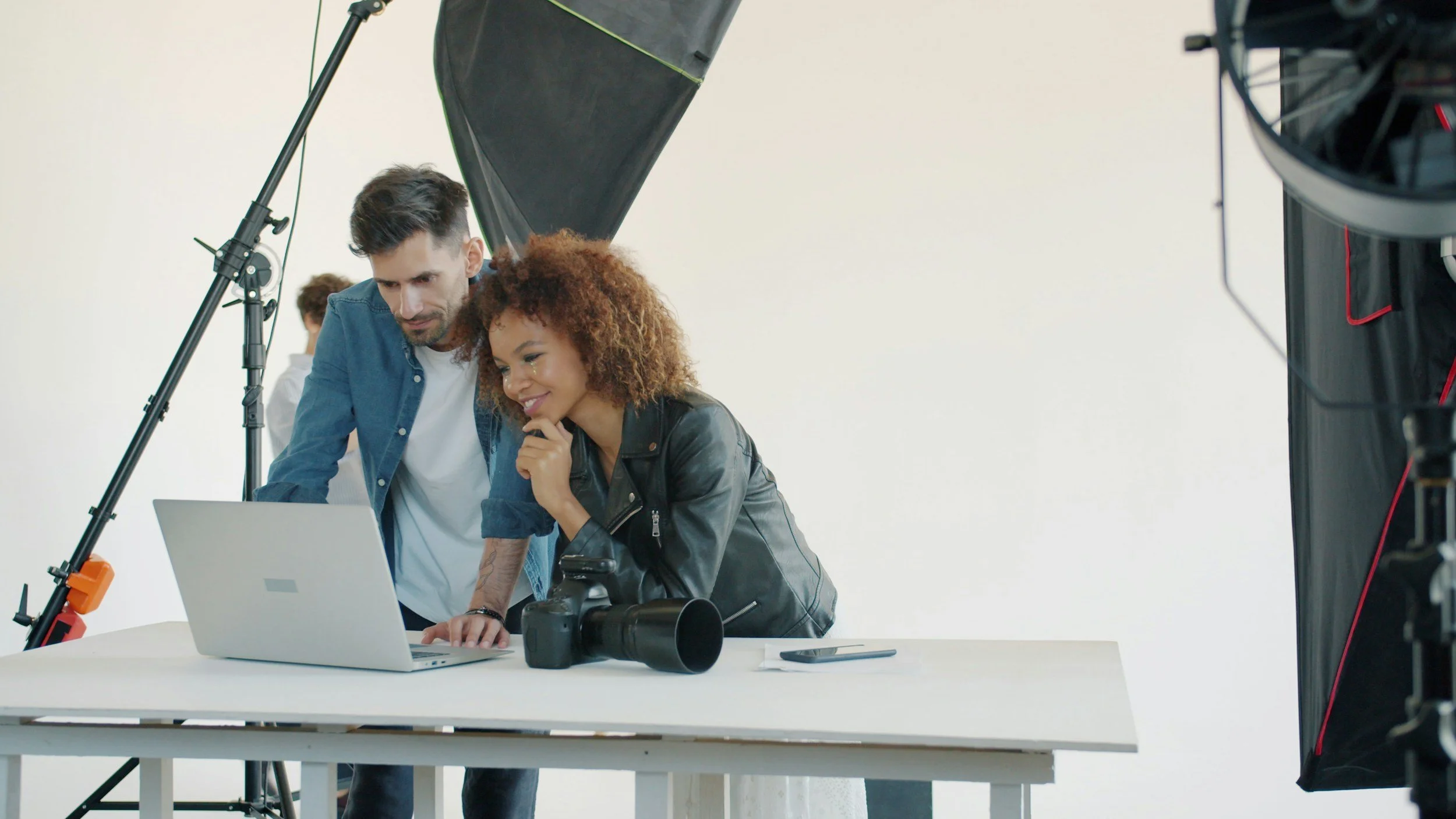 Two people, a man and a woman, looking at a laptop screen in a photo studio, surrounded by professional lighting equipment.