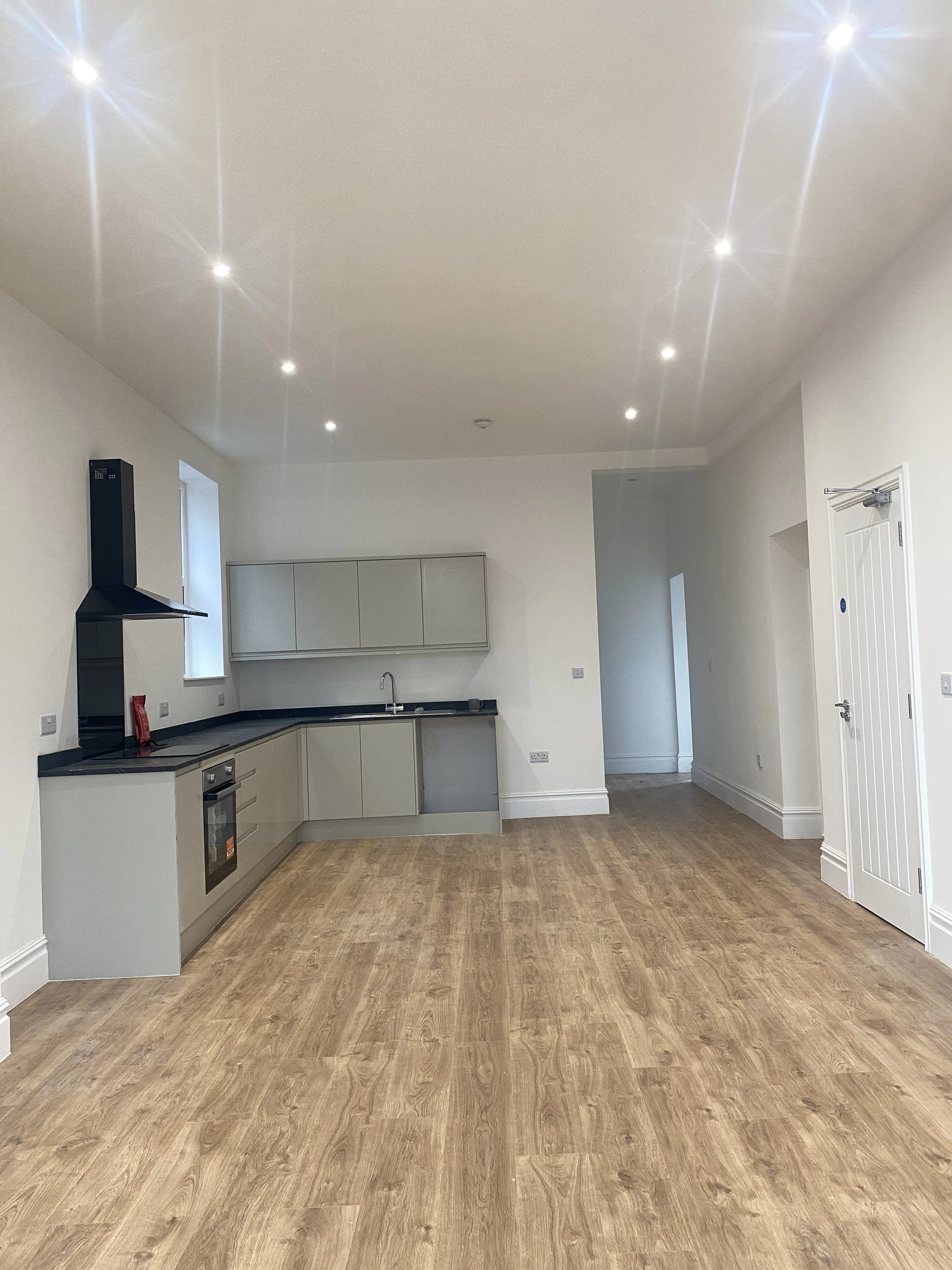 Empty modern kitchen with wood flooring, white walls, and a ceiling with multiple recessed lights.