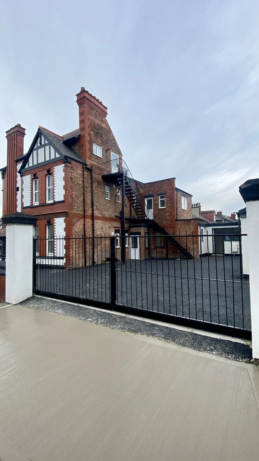 A brick building with a black metal fire escape and a gated yard, under a cloudy sky.
