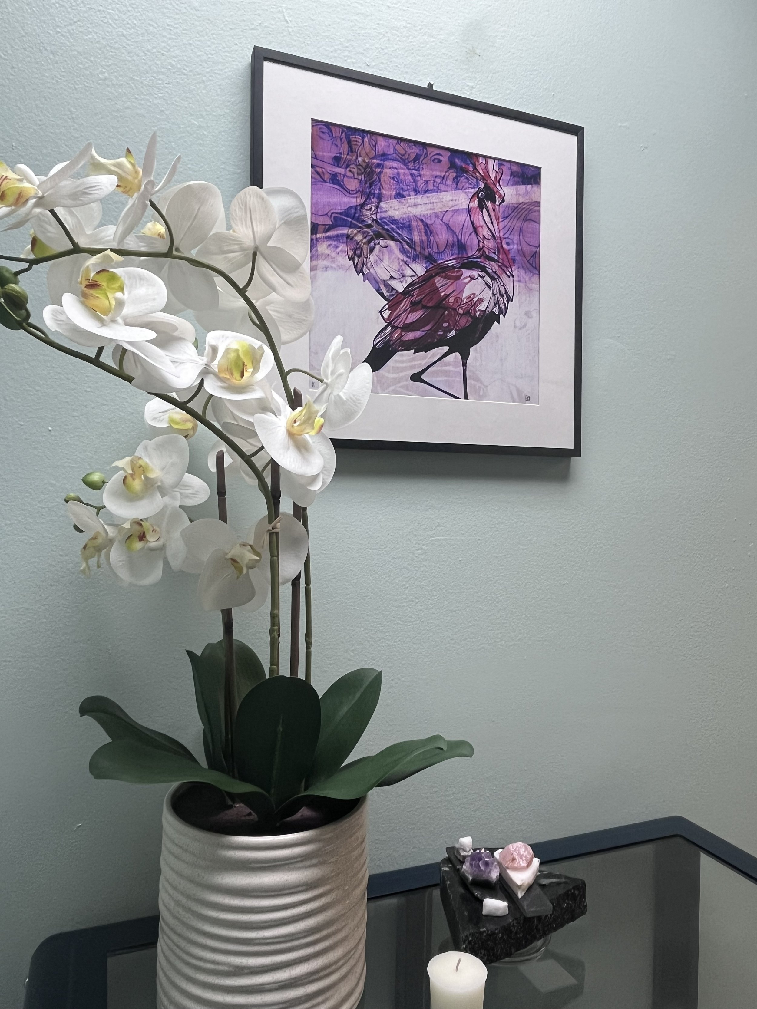 White orchid and framed purple heron artwork in a calm treatment room at Blossom Wellness Centre