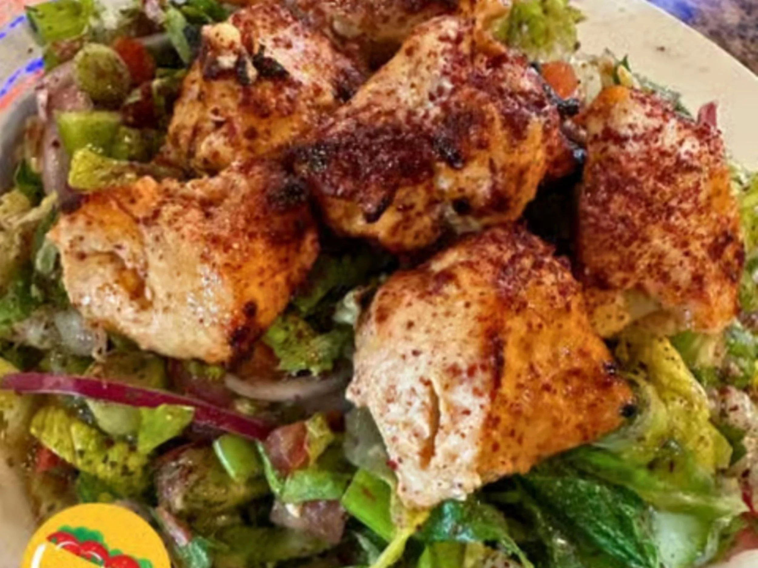 Close-up of grilled chicken pieces seasoned with spices, served on a bed of leafy greens and vegetables.