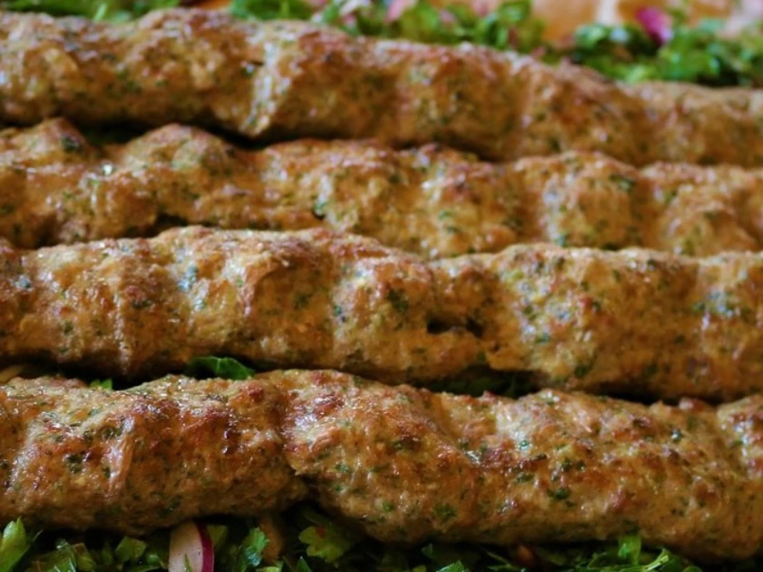 Close-up of three grilled burgers with herbs, on a bed of greens.