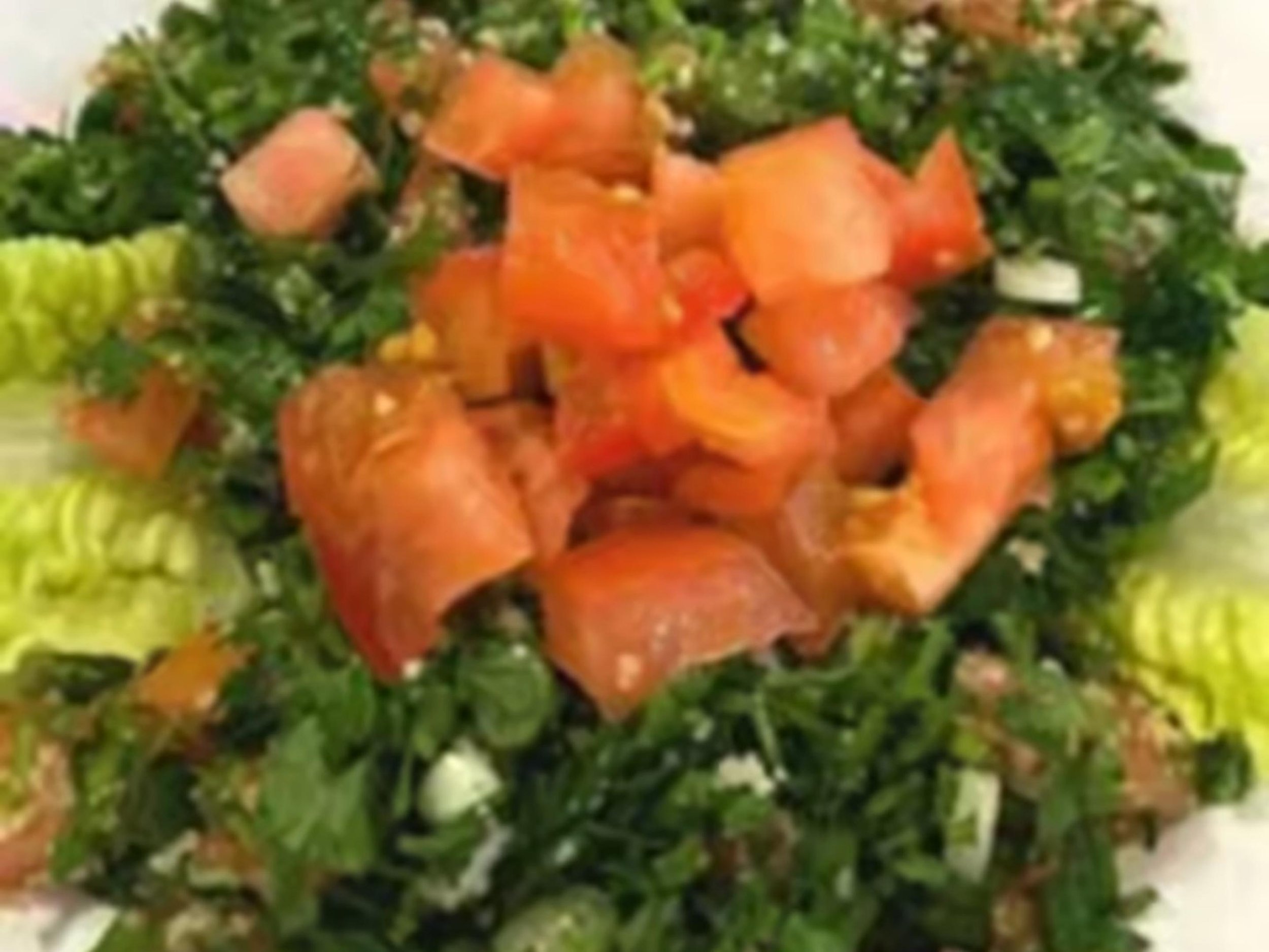 Close-up of a salad with diced tomatoes, chopped greens, and chopped onions.
