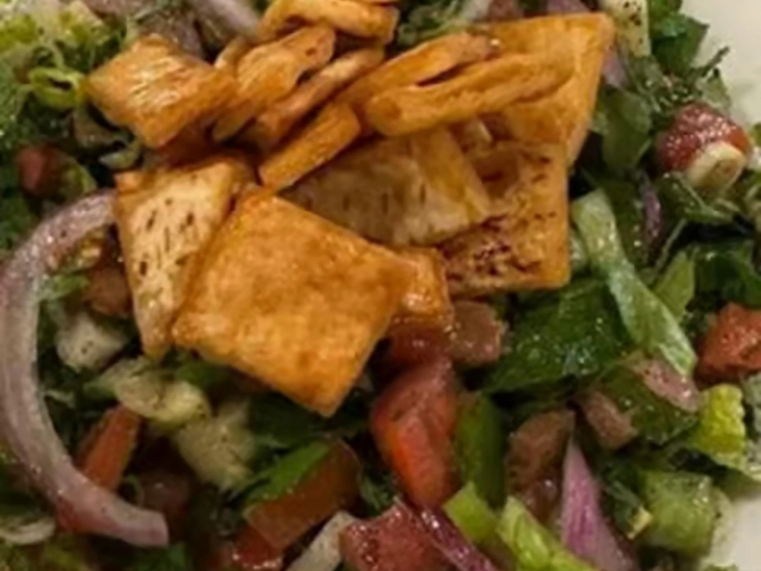 Close-up of a salad with grilled chicken strips, strawberries, vegetables, and leafy greens.