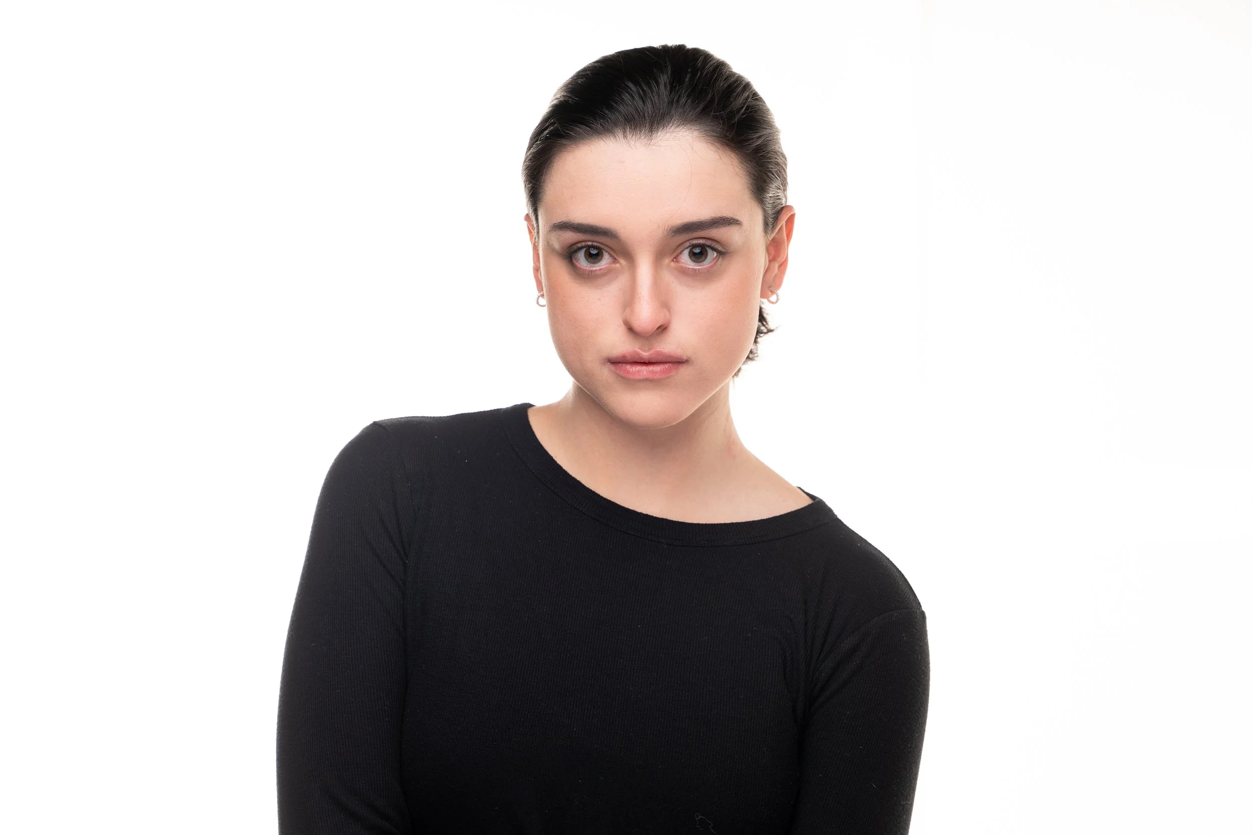 A young woman with dark hair and light skin wearing a black top, looking directly at the camera with a neutral expression, against a white background.