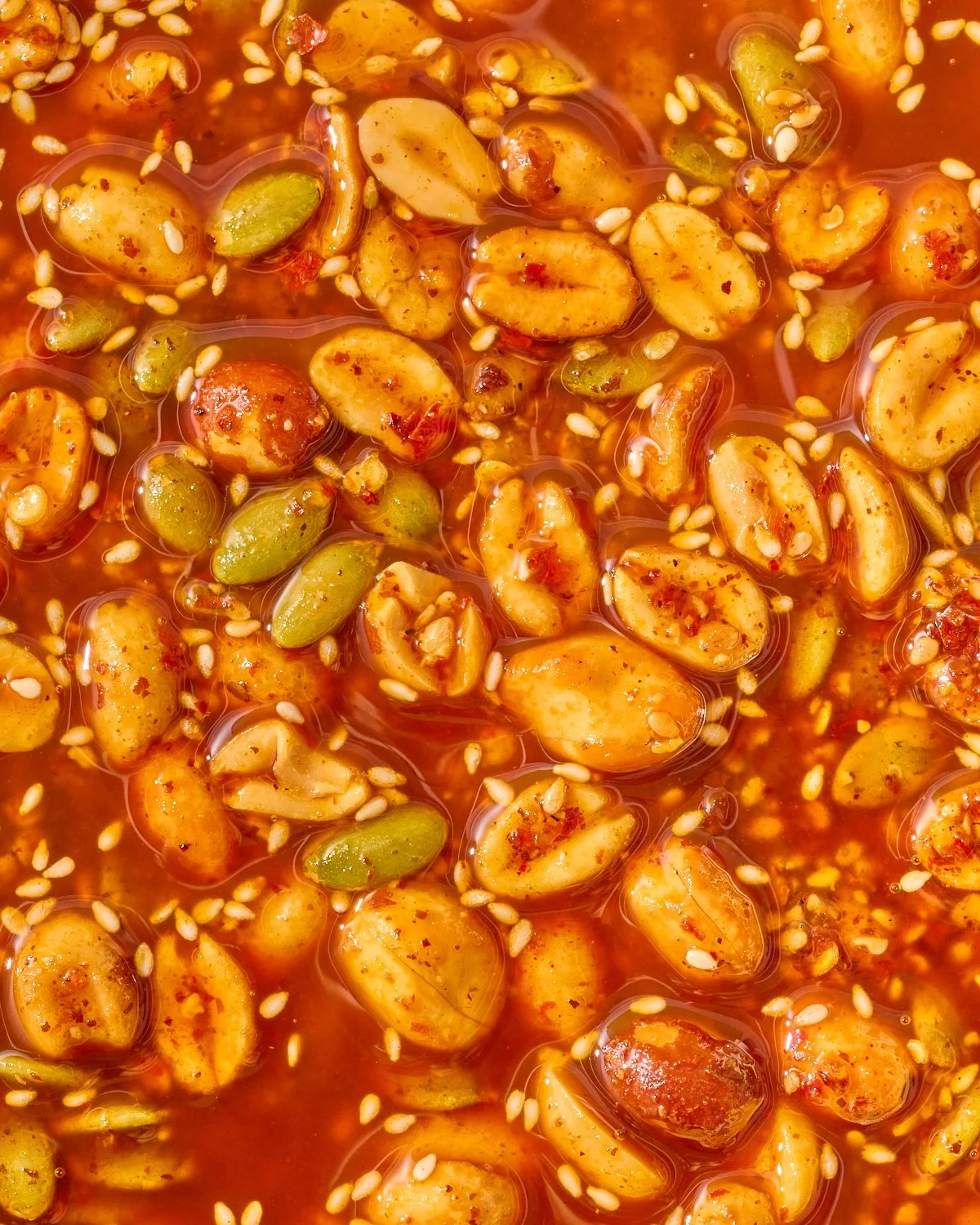 Close-up of a spicy mixed nuts snack with peanuts, pumpkin seeds, and sesame seeds in a red chili sauce.