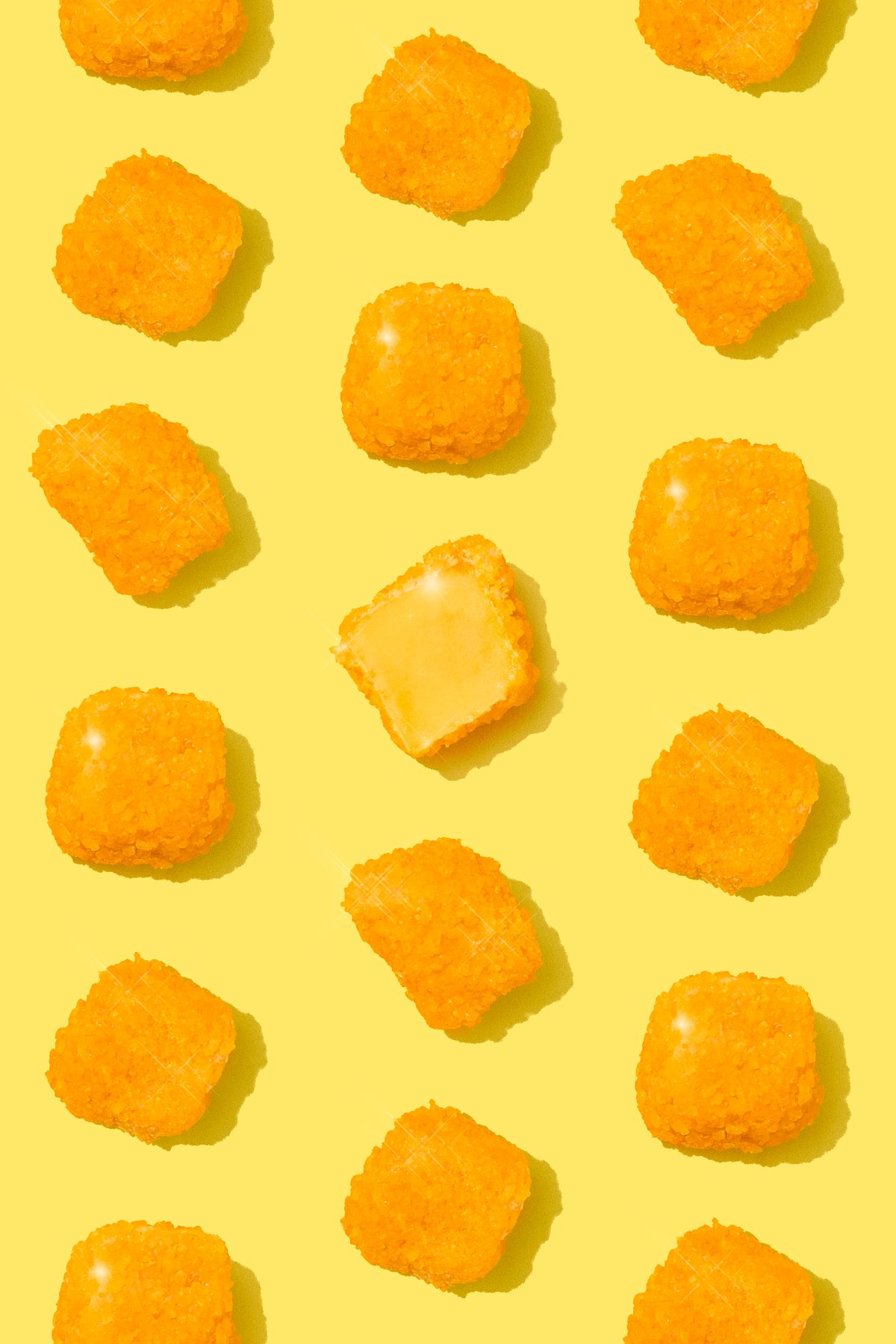 Multiple pieces of orange-colored food, possibly fried chicken nuggets, on a yellow background, with one piece cut in half showing the inside.