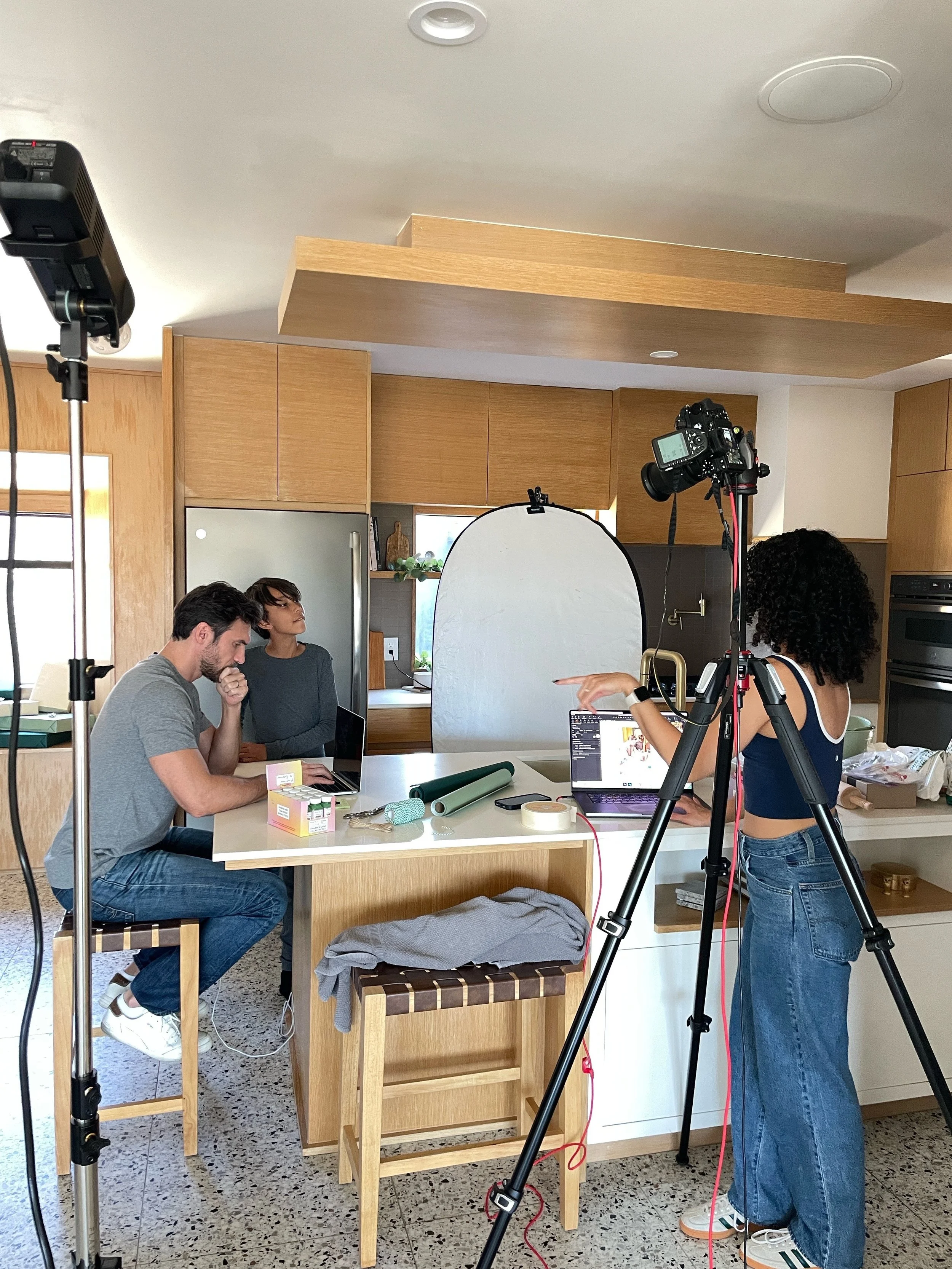 People preparing for a photoshoot or video shoot in a kitchen setting with cameras, lighting, and a backdrop.