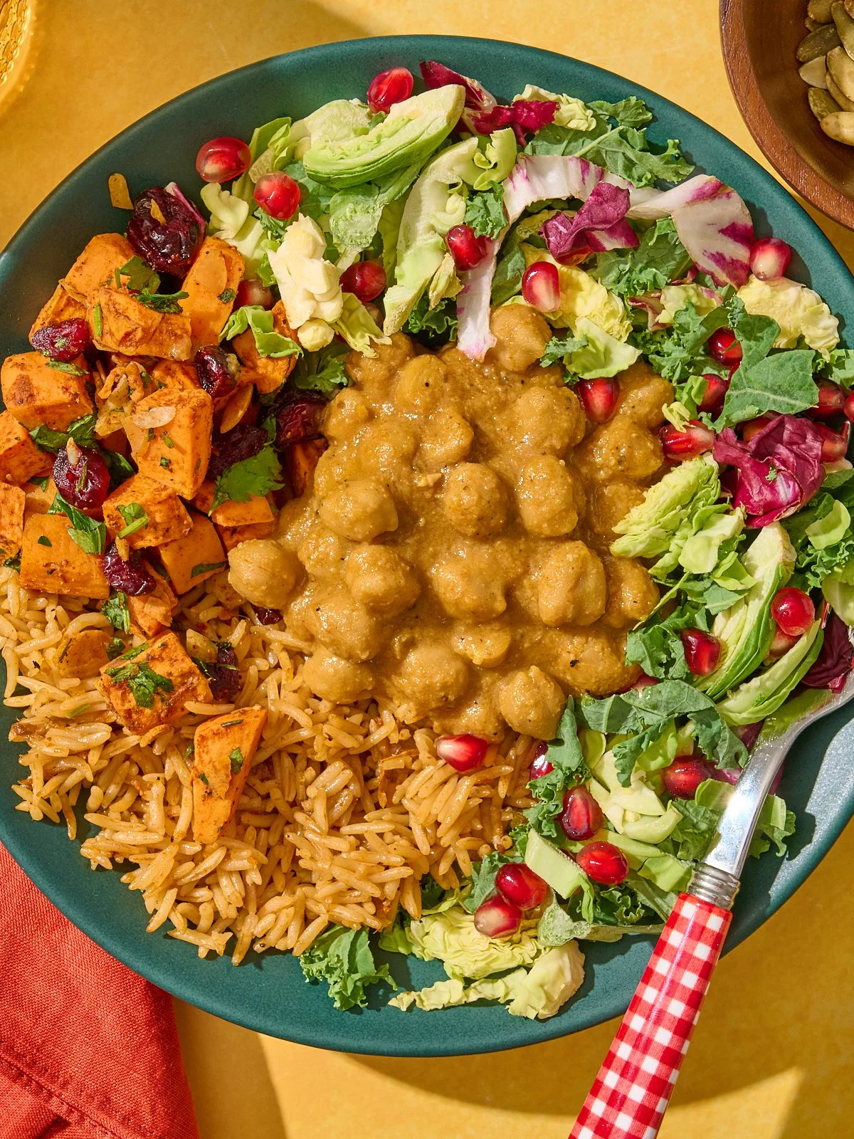 A plate of food with rice, seasoned tofu, chickpea stew, and fresh salad with pomegranate seeds.
