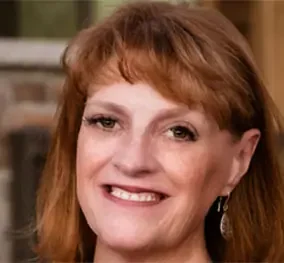 Close-up of a woman with red hair smiling and wearing earrings.