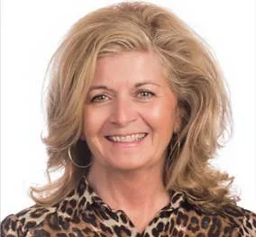 A woman with blonde, voluminous hair smiling, wearing a leopard print top.