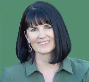 A woman with shoulder-length black hair, wearing a green blouse and earrings, smiling against a green background.