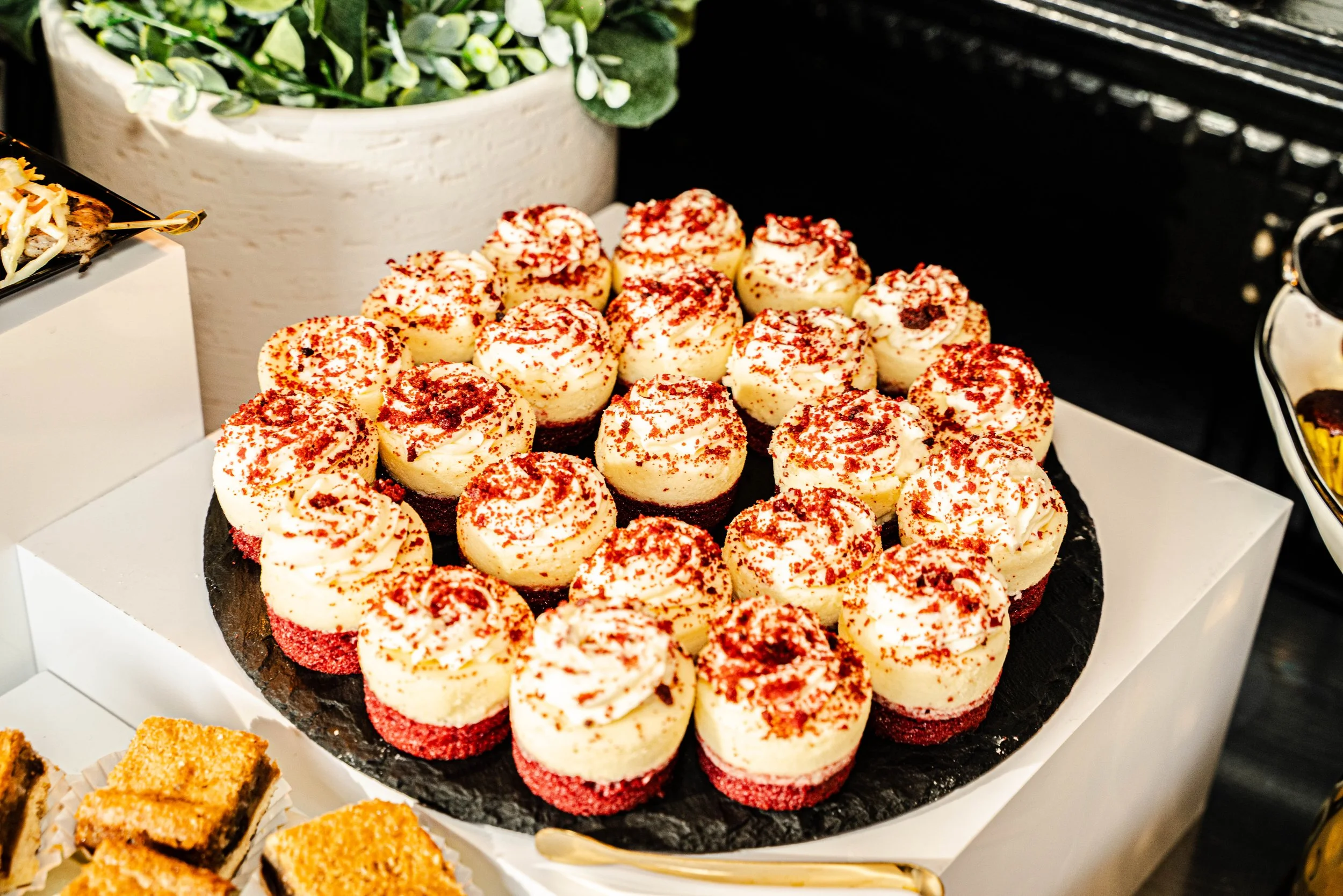 Plate of assorted cheesecake bites topped with red sprinkles on black slate serving platter.