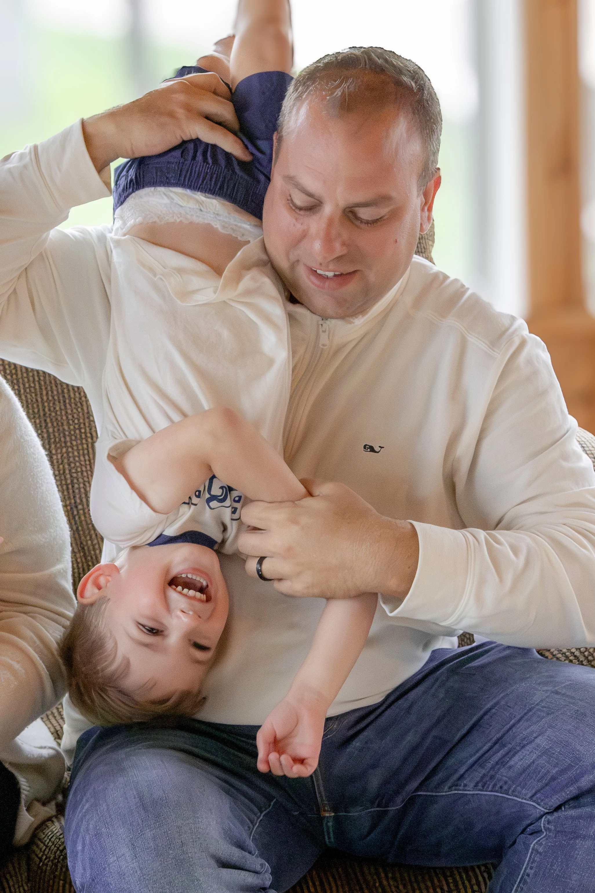 A man and a young boy lying on the floor, playing and laughing together, with the man holding the boy under his arm.