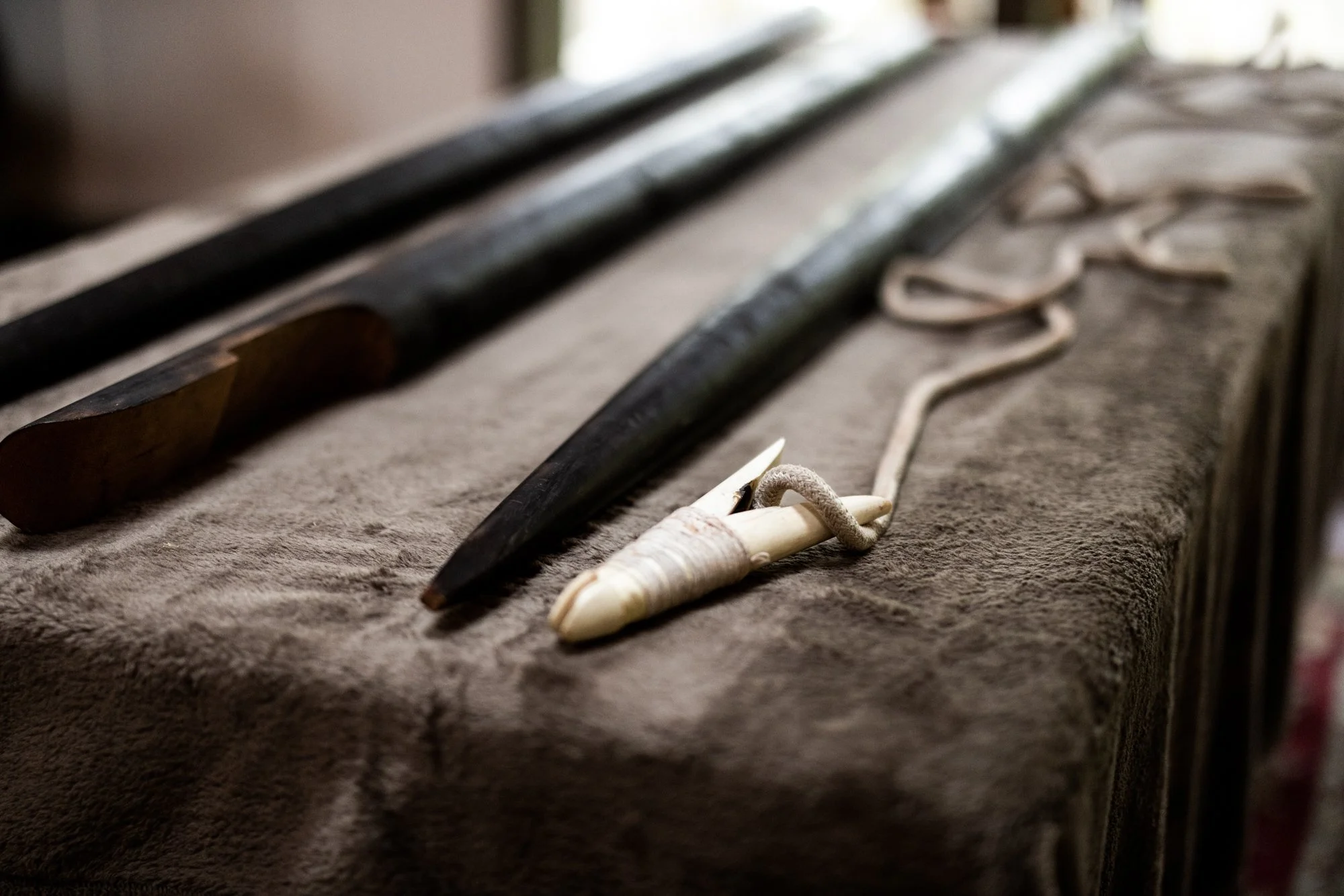 A traditional Nuu-chah-nulth whaling harpoon displayed on a rough surface, with a blurred background of a window and natural light.