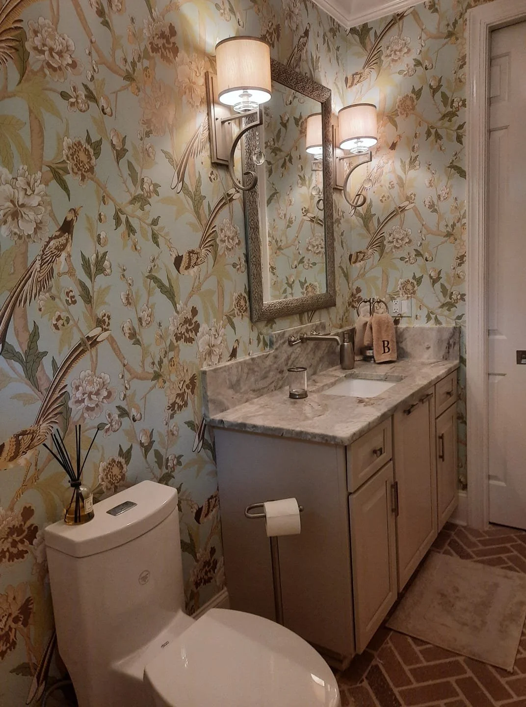 Powder room with botanical bird wallpaper, framed mirror, and wall sconces designed by Bonnie Boyette Designs