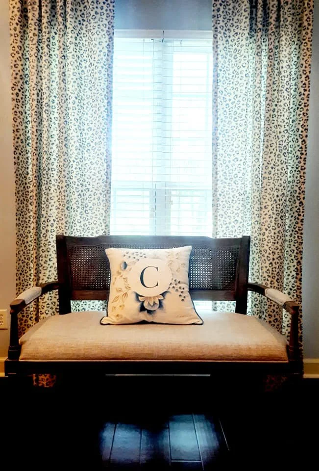 Window nook with a black wood bench, monogrammed pillow, and floral drapery panels designed by Bonnie Boyette Designs