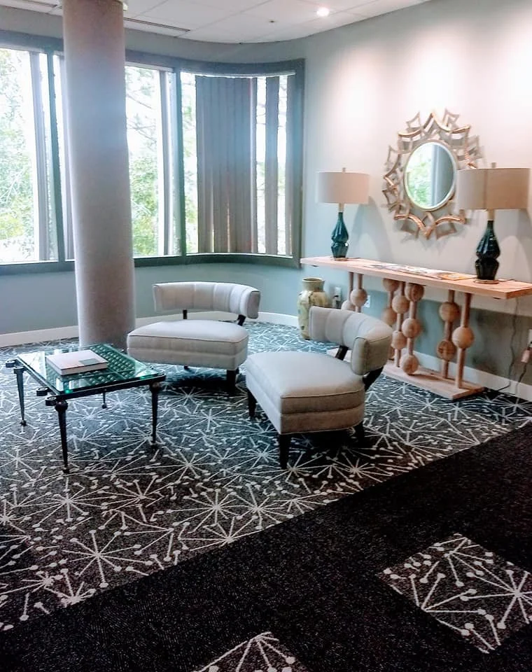 Bright living area with white accent chairs, a black and white patterned rug, and a gold sunburst mirror designed by Bonnie Boyette Designs