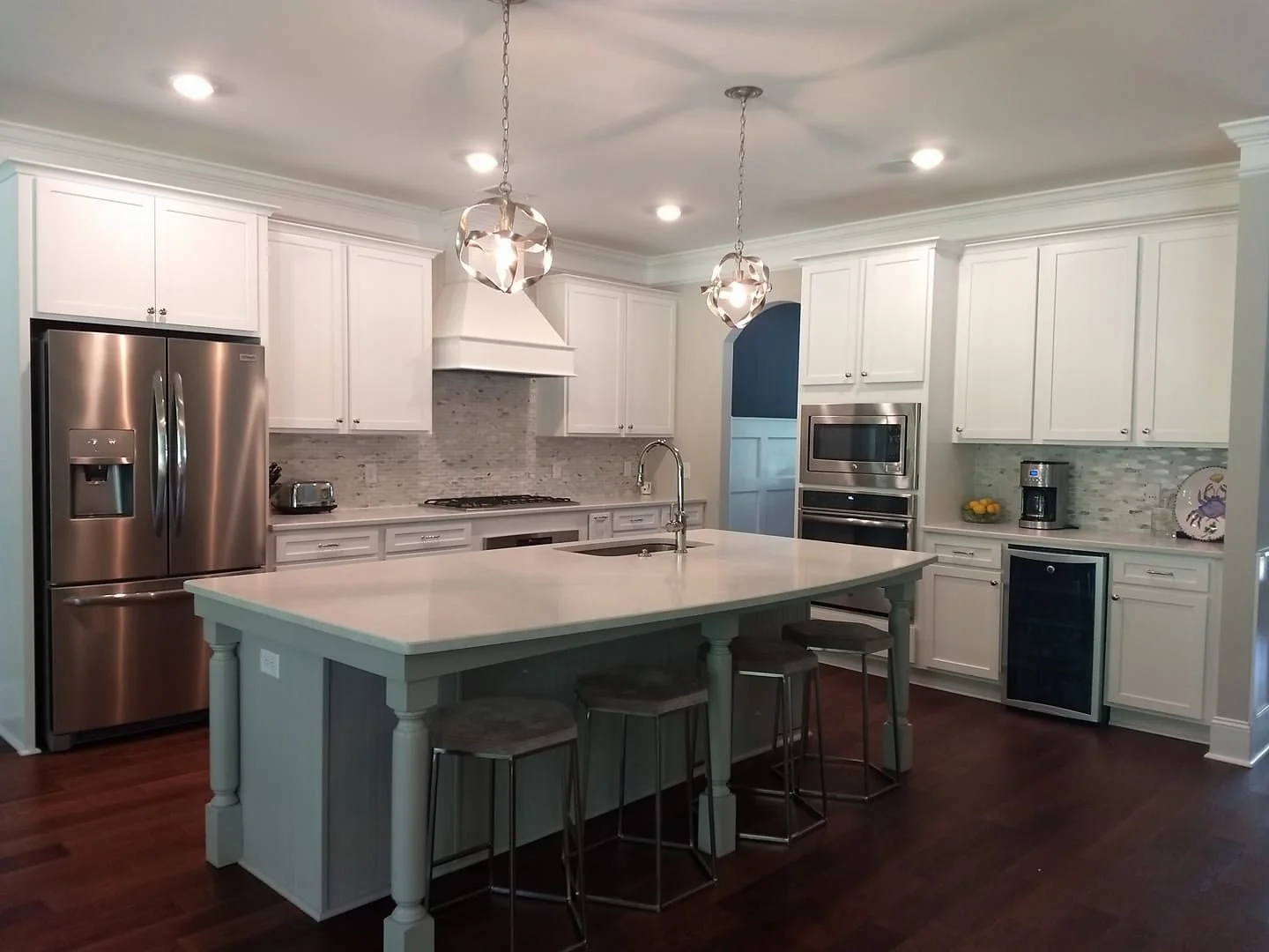 Kitchen with white cabinets, a large gray island with seating, and stainless appliances designed by Bonnie Boyette Designs