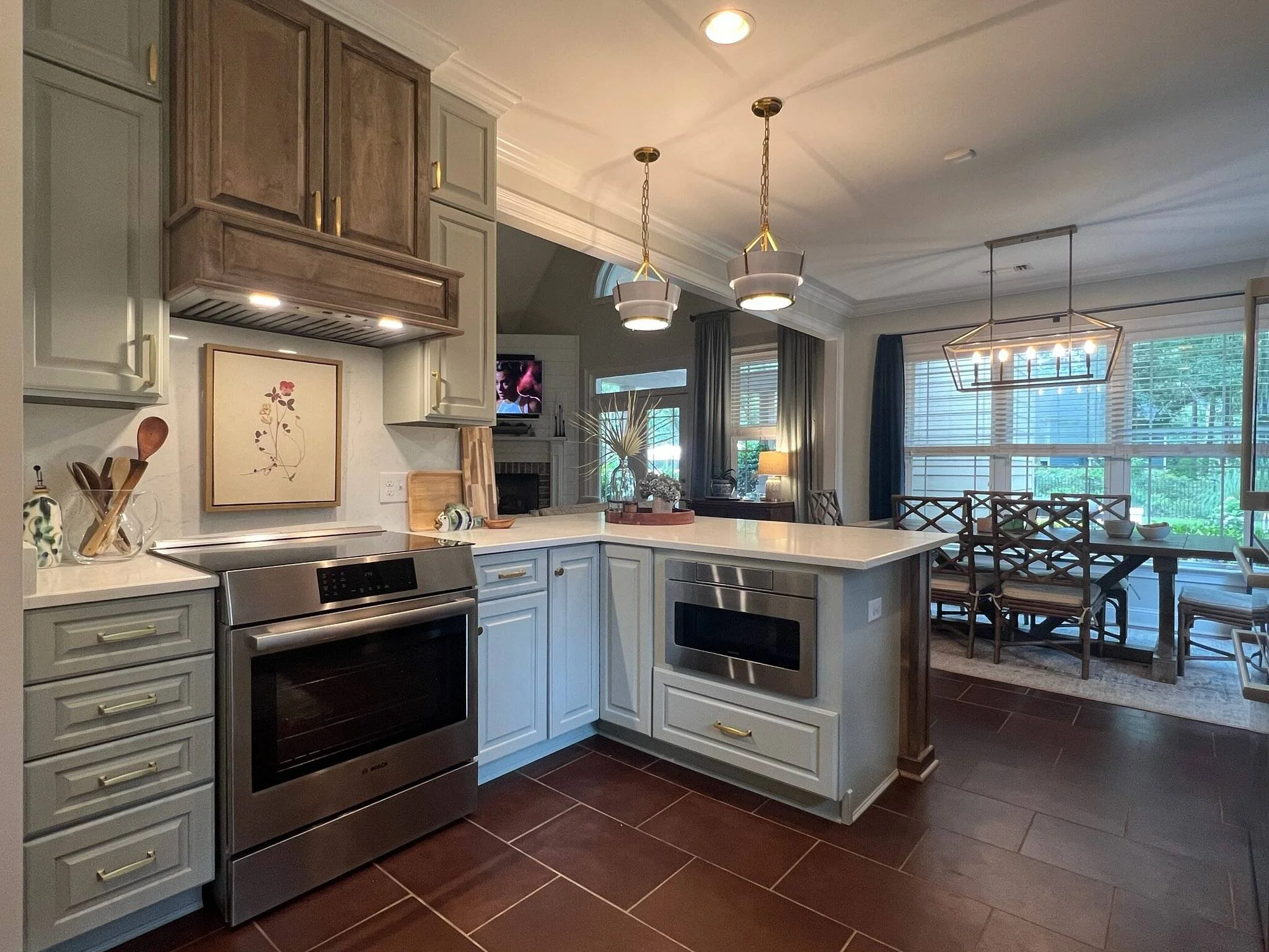 Open kitchen with gray cabinets, a peninsula, and pendant lights leading to a sunny dining area designed by Bonnie Boyette Designs